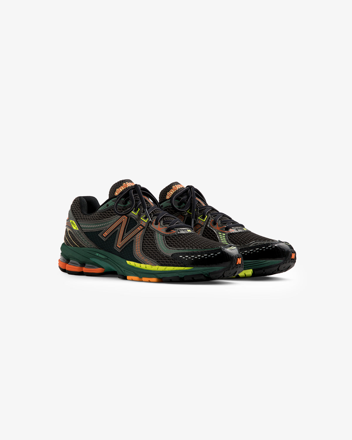 A pair of ALD / New Balance 860v2 sneakers in black with orange and green accents on a white background.