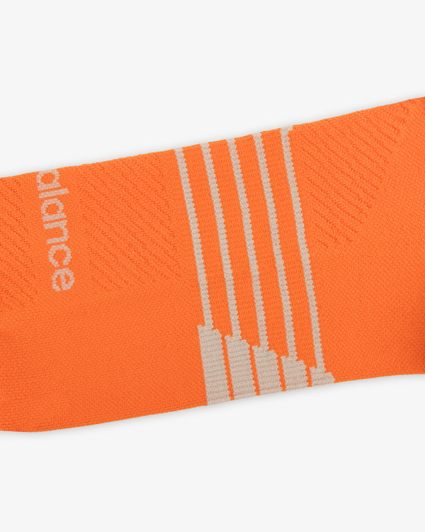 Close-up of ALD / New Balance Running Crew Sock—orange with white stripes and partial white text on the side.