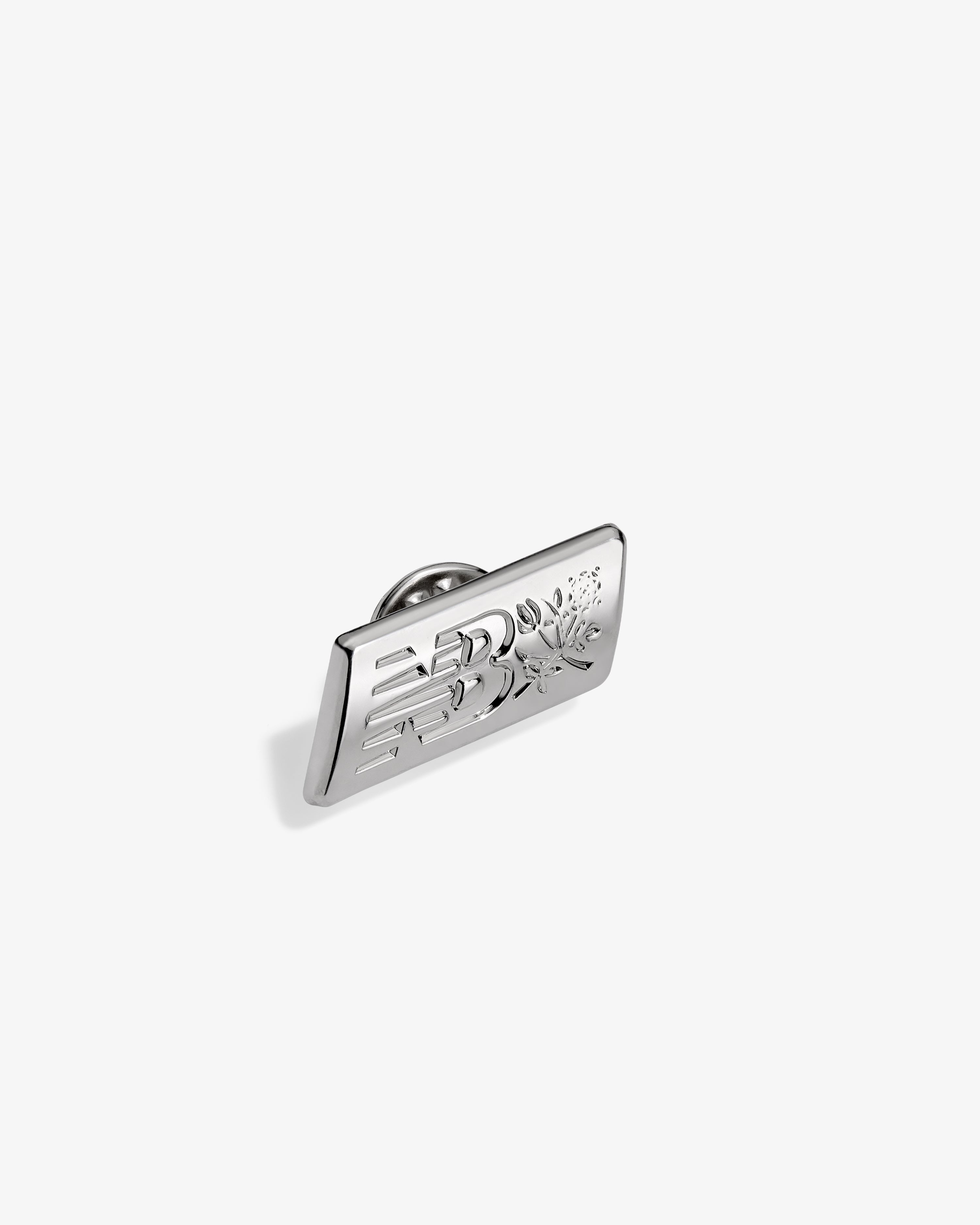 ALD / New Balance Logo Pin, rectangular silver with engraved design, shown on a plain white background.