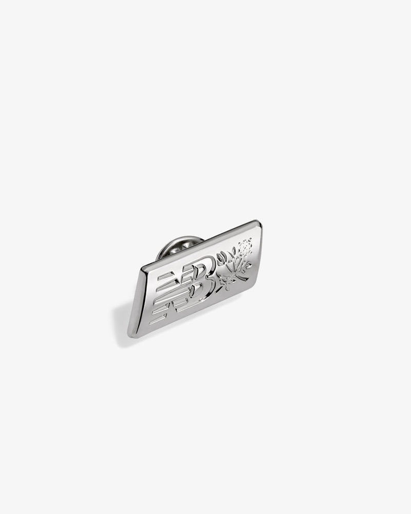 ALD / New Balance Logo Pin, rectangular silver with engraved design, shown on a plain white background.