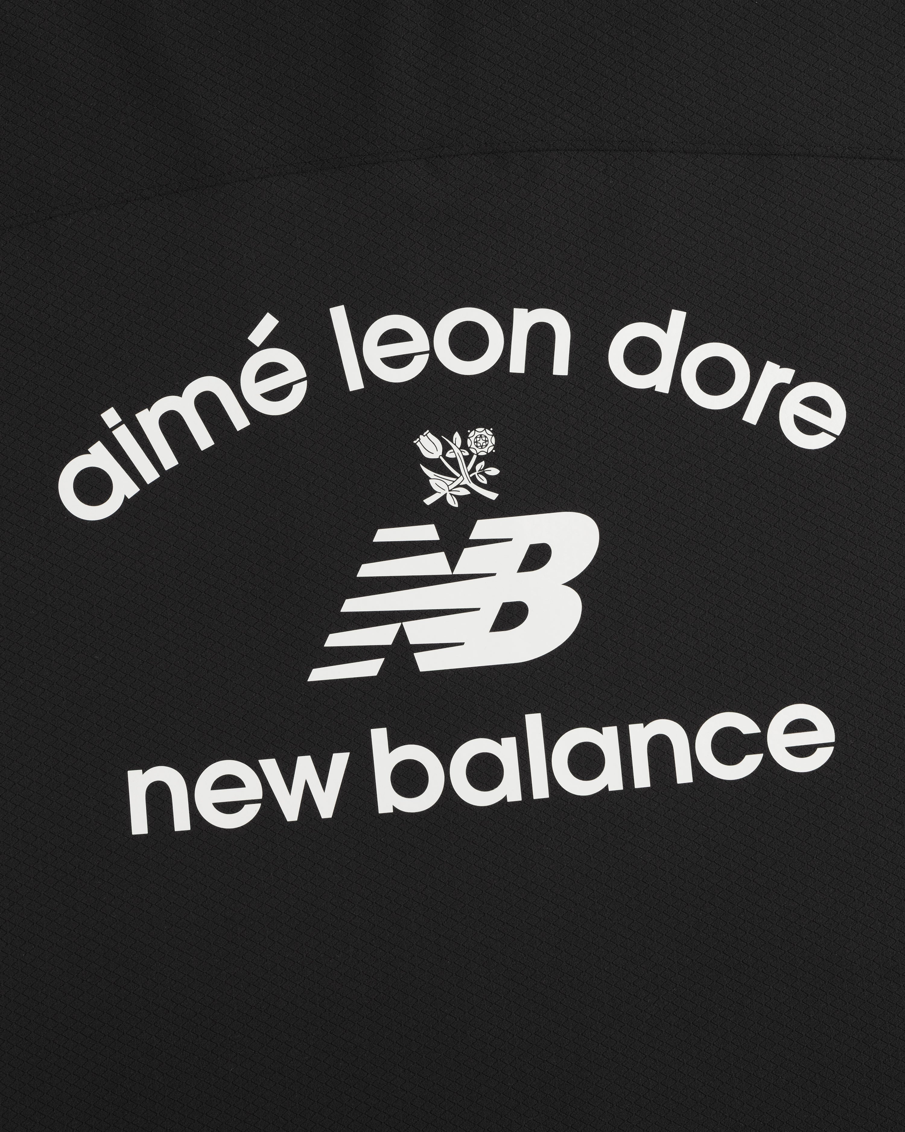 Black ALD / New Balance Full-Zip Warmup Hoodie with white arched text and small floral graphic on black fabric.