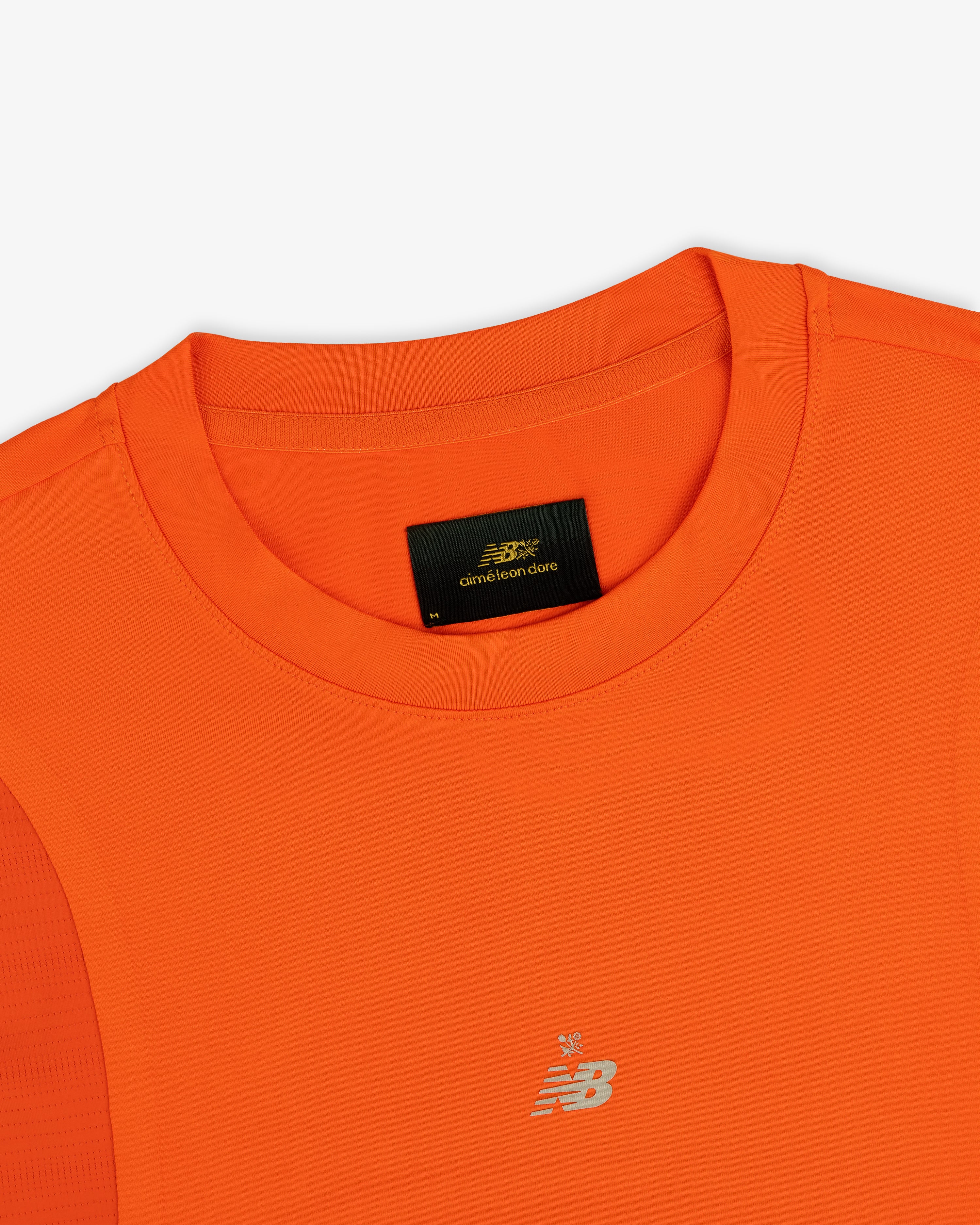 Close-up of an orange ALD / New Balance Performance Long-Sleeve Tee with crew neck and black label inside the collar.