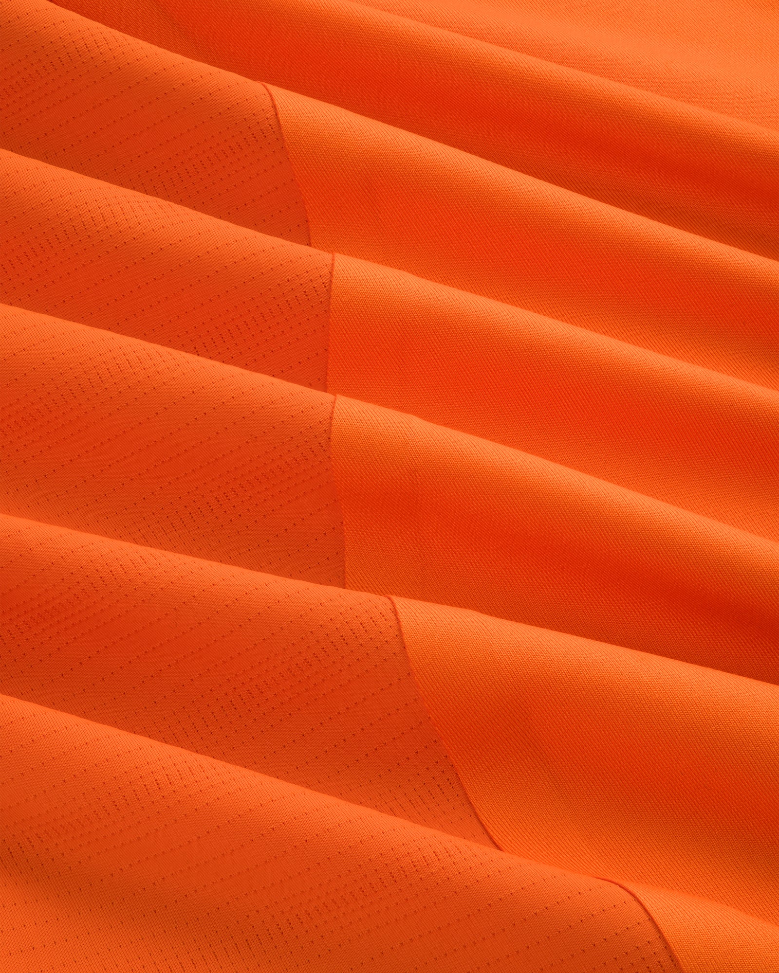 Close-up of the ALD / New Balance Performance Long-Sleeve Tee's orange fabric with diagonal lines and textured folds.
