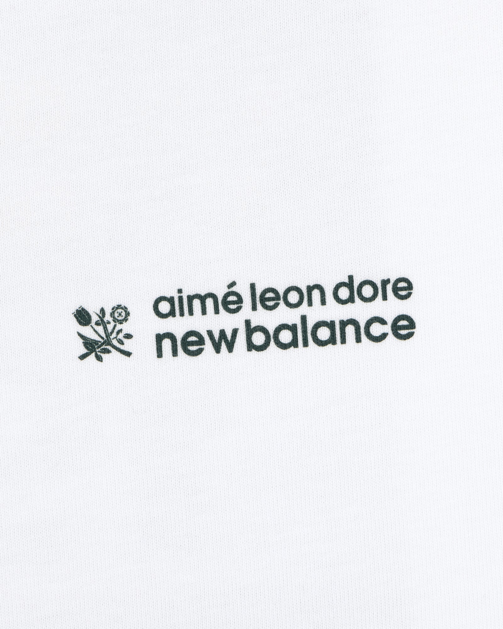 Black ALD / New Balance Running Bib Tee with logo and small flower graphic on white fabric background.