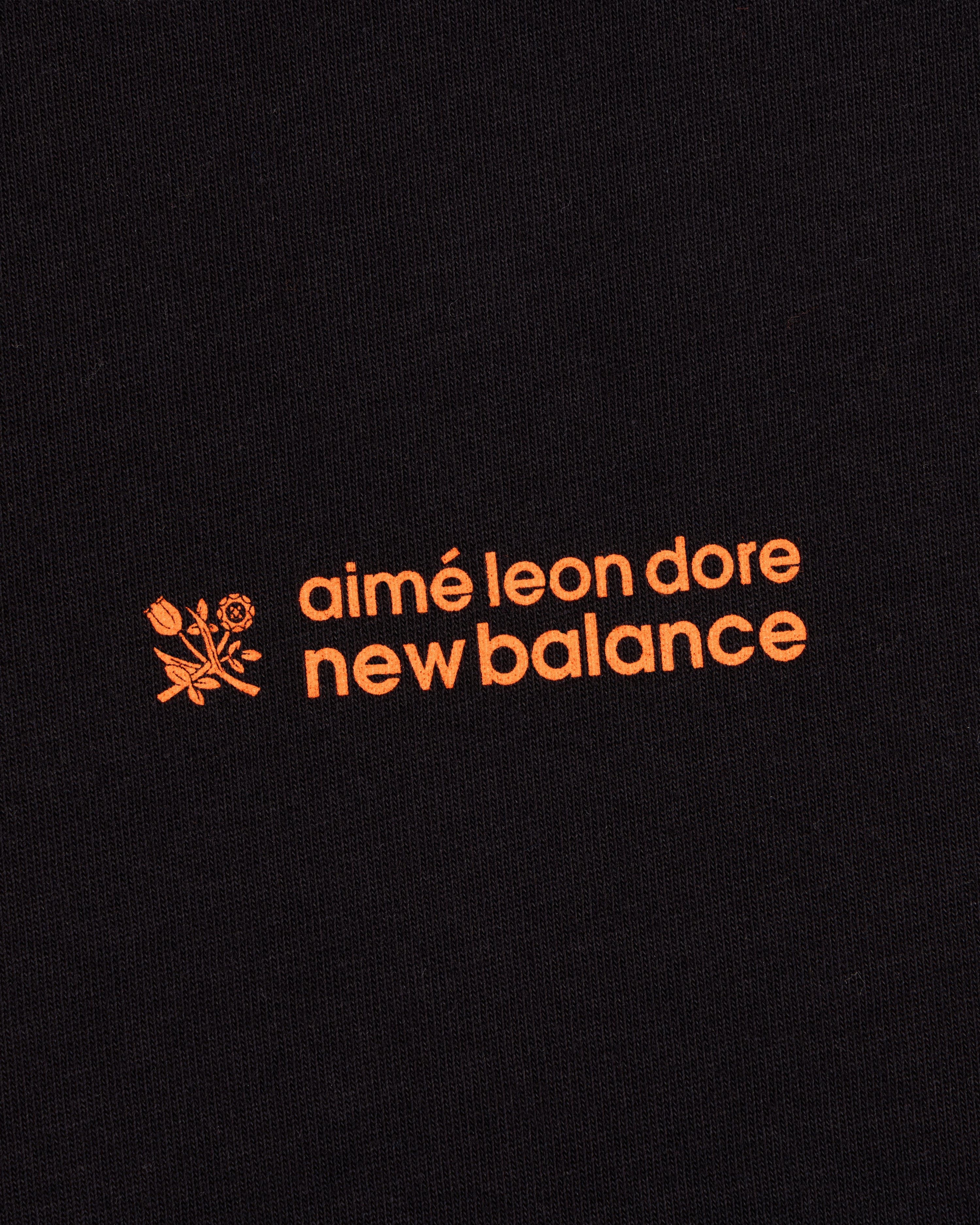 ALD / New Balance Running Bib Tee features an orange logo with a flower graphic on black fabric.