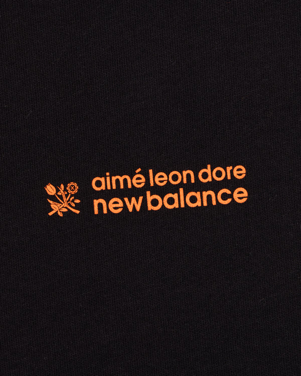 ALD / New Balance Running Bib Tee features an orange logo with a flower graphic on black fabric.
