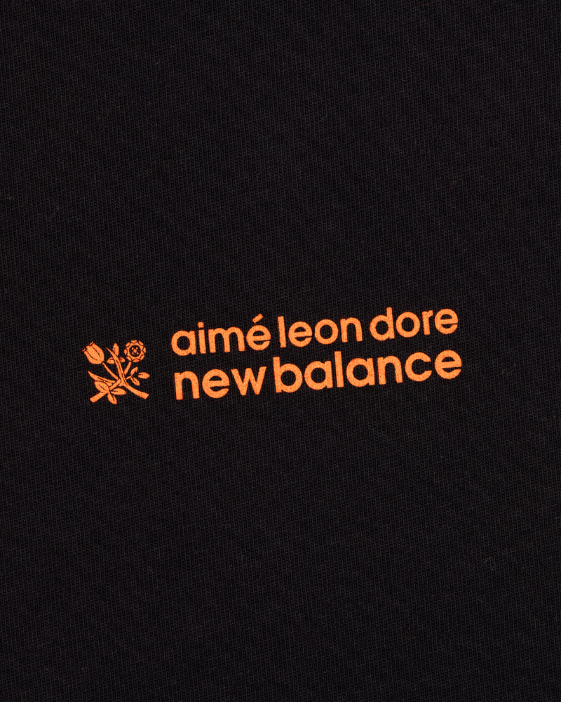 ALD / New Balance Running Bib Tee features an orange logo with a flower graphic on black fabric.