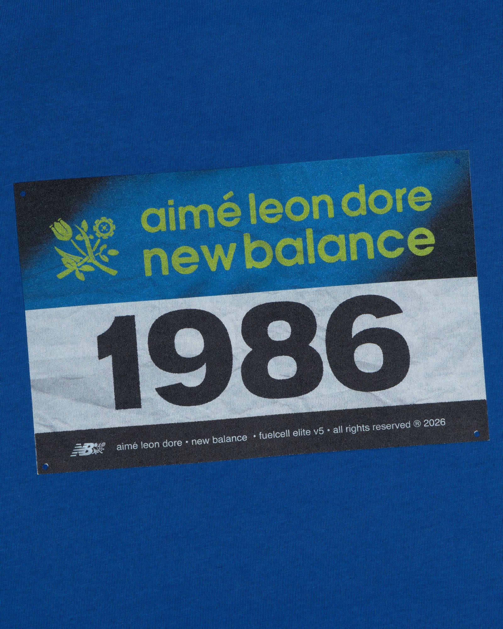 The ALD / New Balance Running Bib Tee features a blue race bib with "aimé leon dore" and 1986 printed on it.