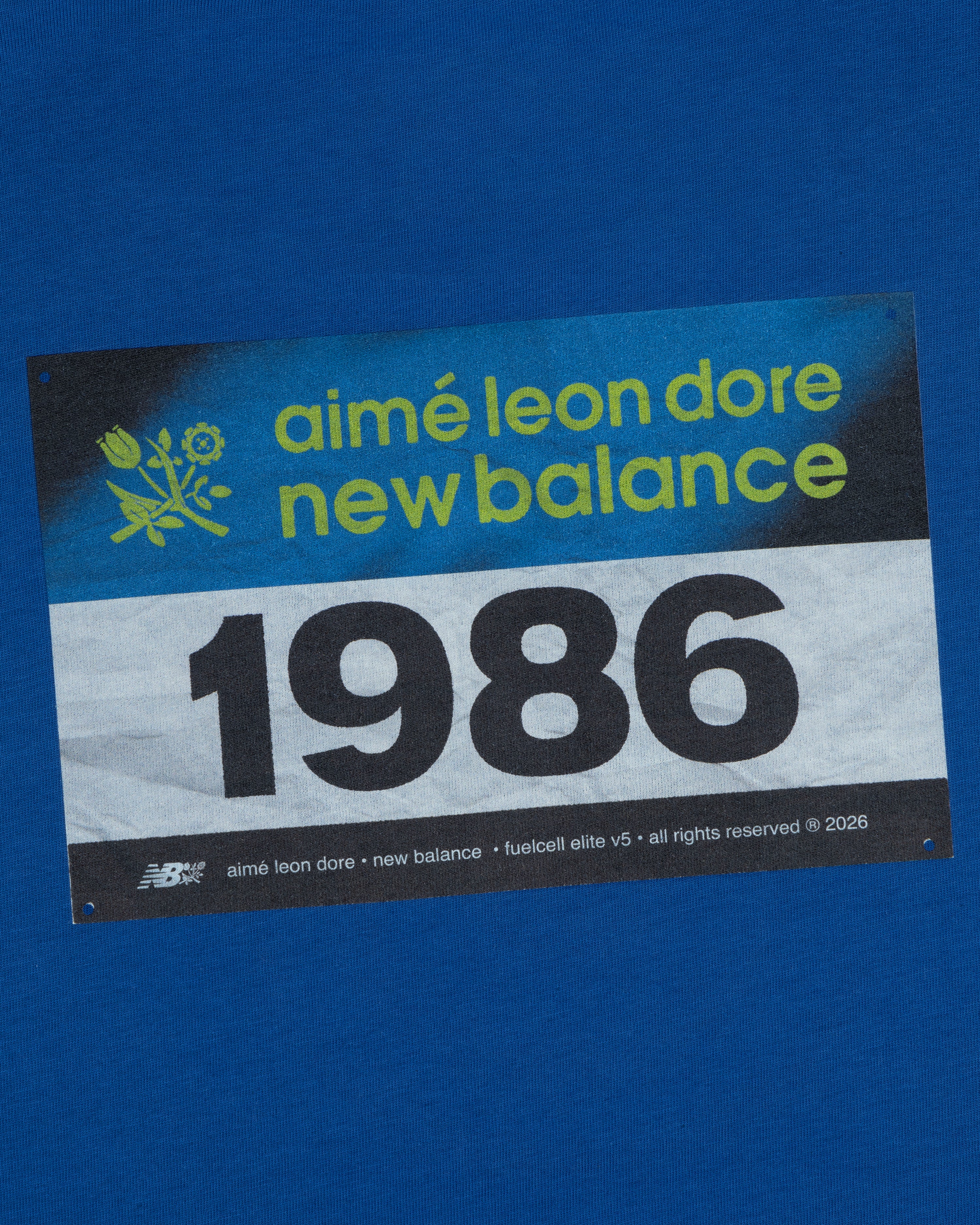 The ALD / New Balance Running Bib Tee features a blue race bib with "aimé leon dore" and 1986 printed on it.