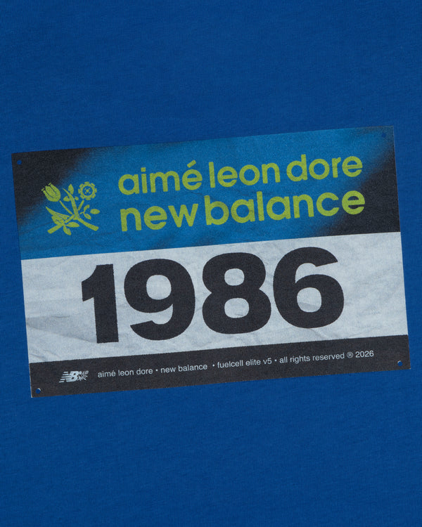 The ALD / New Balance Running Bib Tee features a blue race bib with "aimé leon dore" and 1986 printed on it.