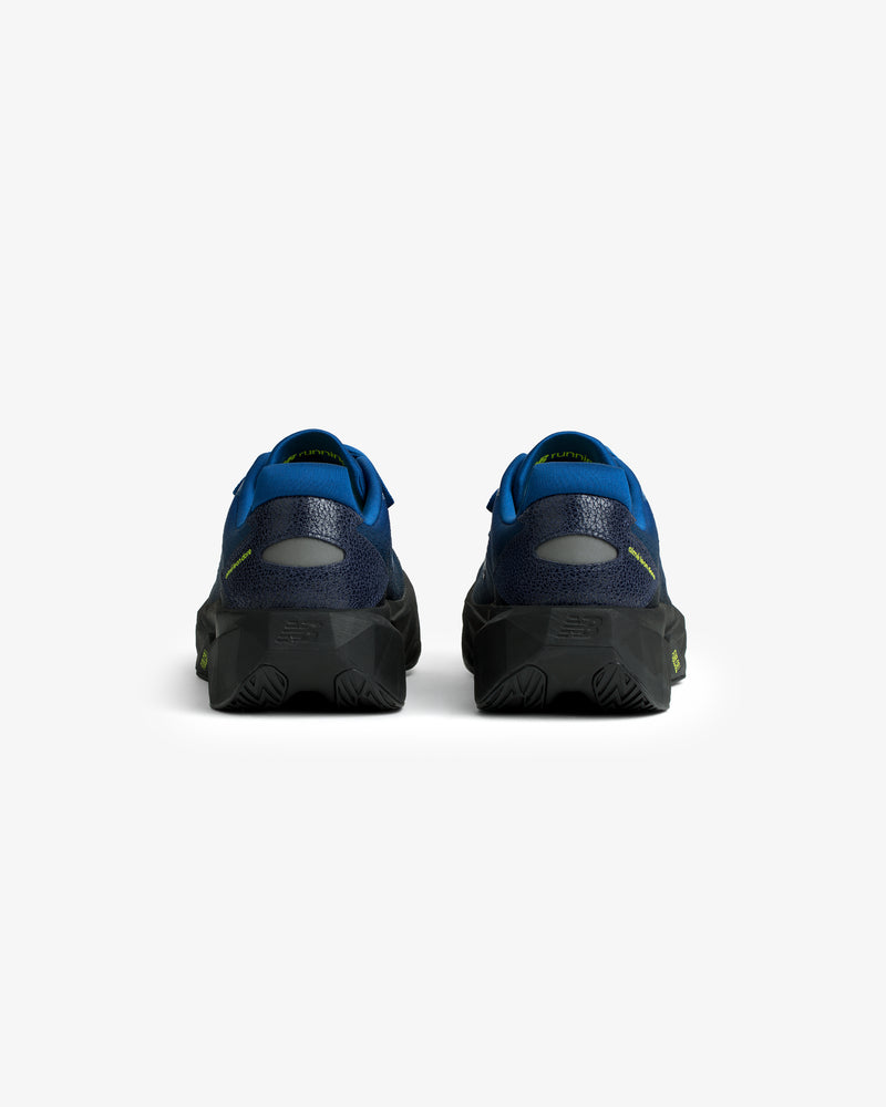 Rear view of ALD / New Balance FuelCell Rebel v5 in blue and black with textured soles on a white background.