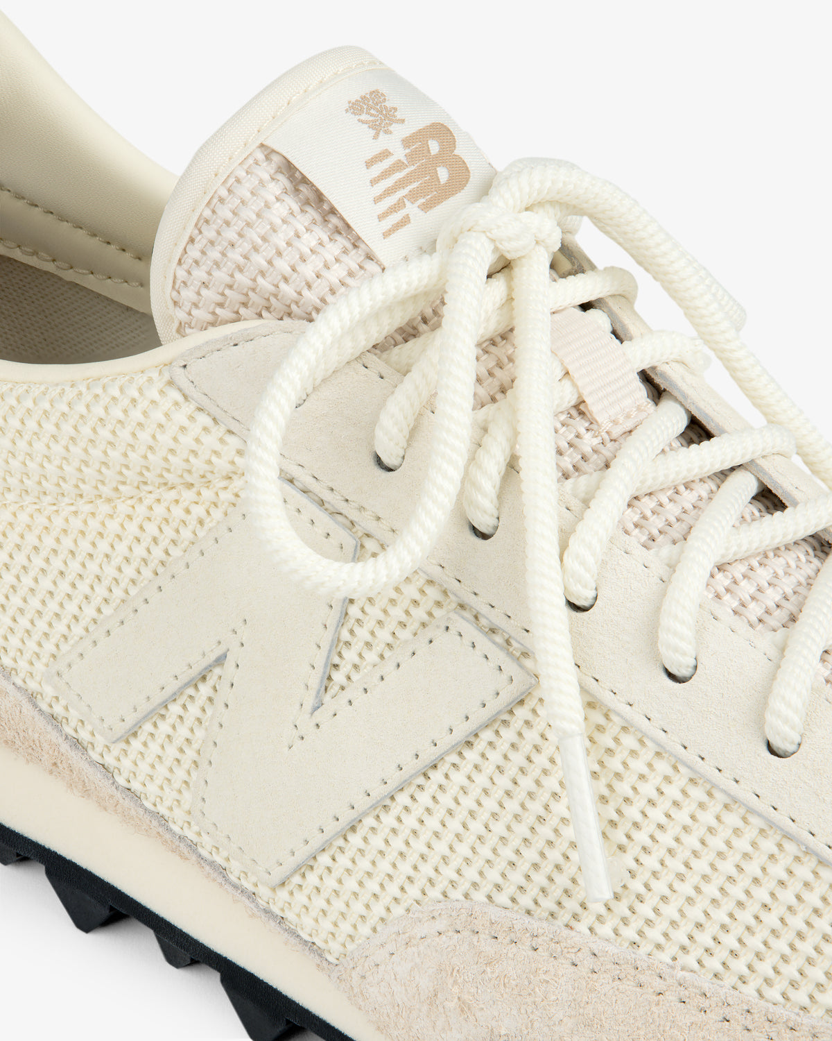 Close-up of the ALD / New Balance Gator sneaker in cream mesh and suede with white laces and a gold logo on the tongue.