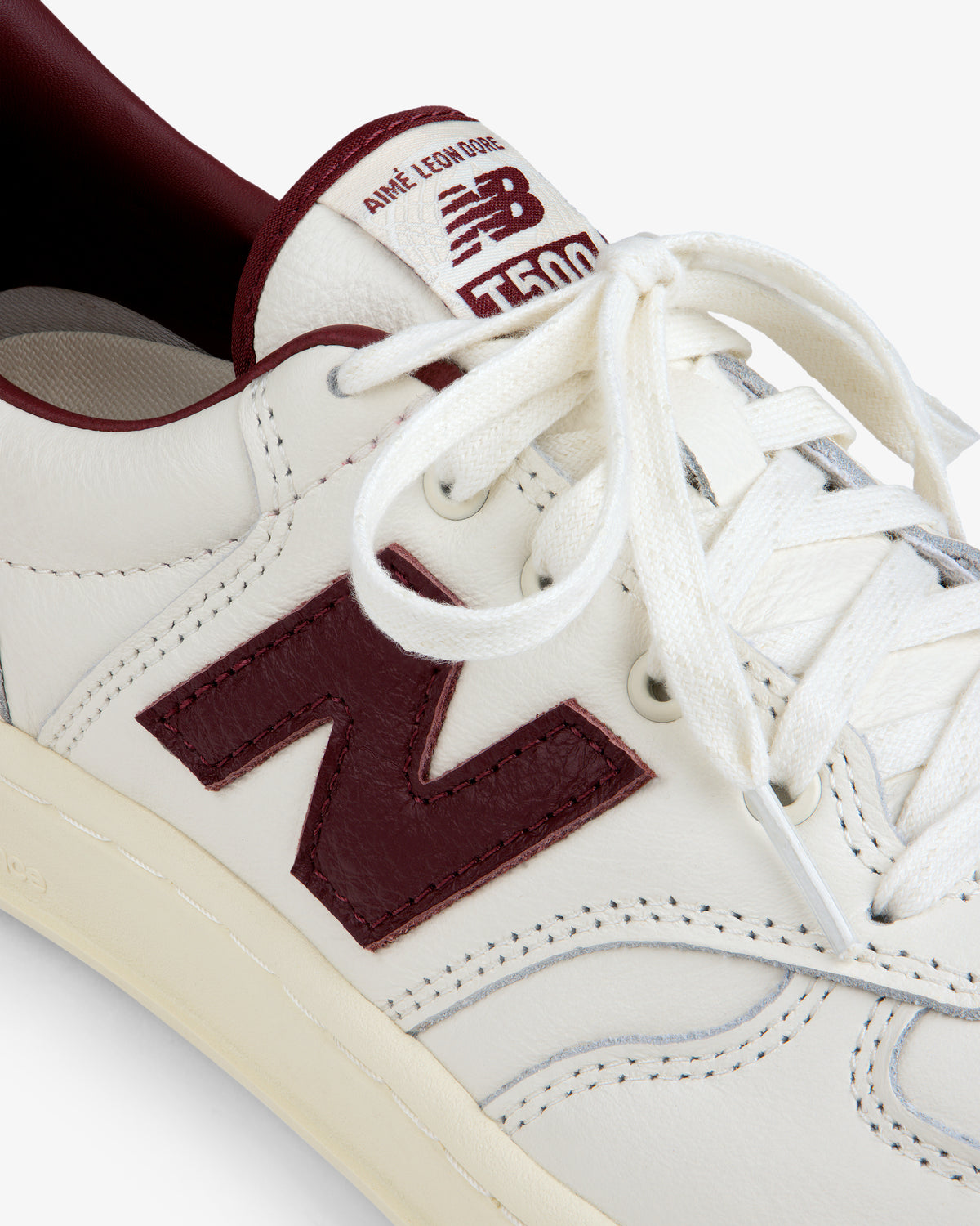 Cream-colored ALD / New Balance T500 Tennis Oxfords with a dark red logo and trim.