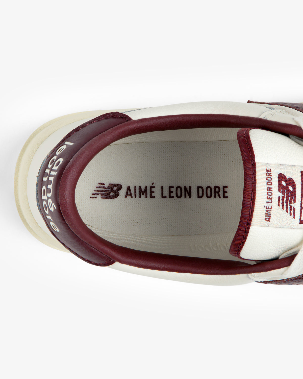 Top-down view of an ALD / New Balance T500 Tennis Oxford white sneaker with red trim and logos on the insole and tongue.
