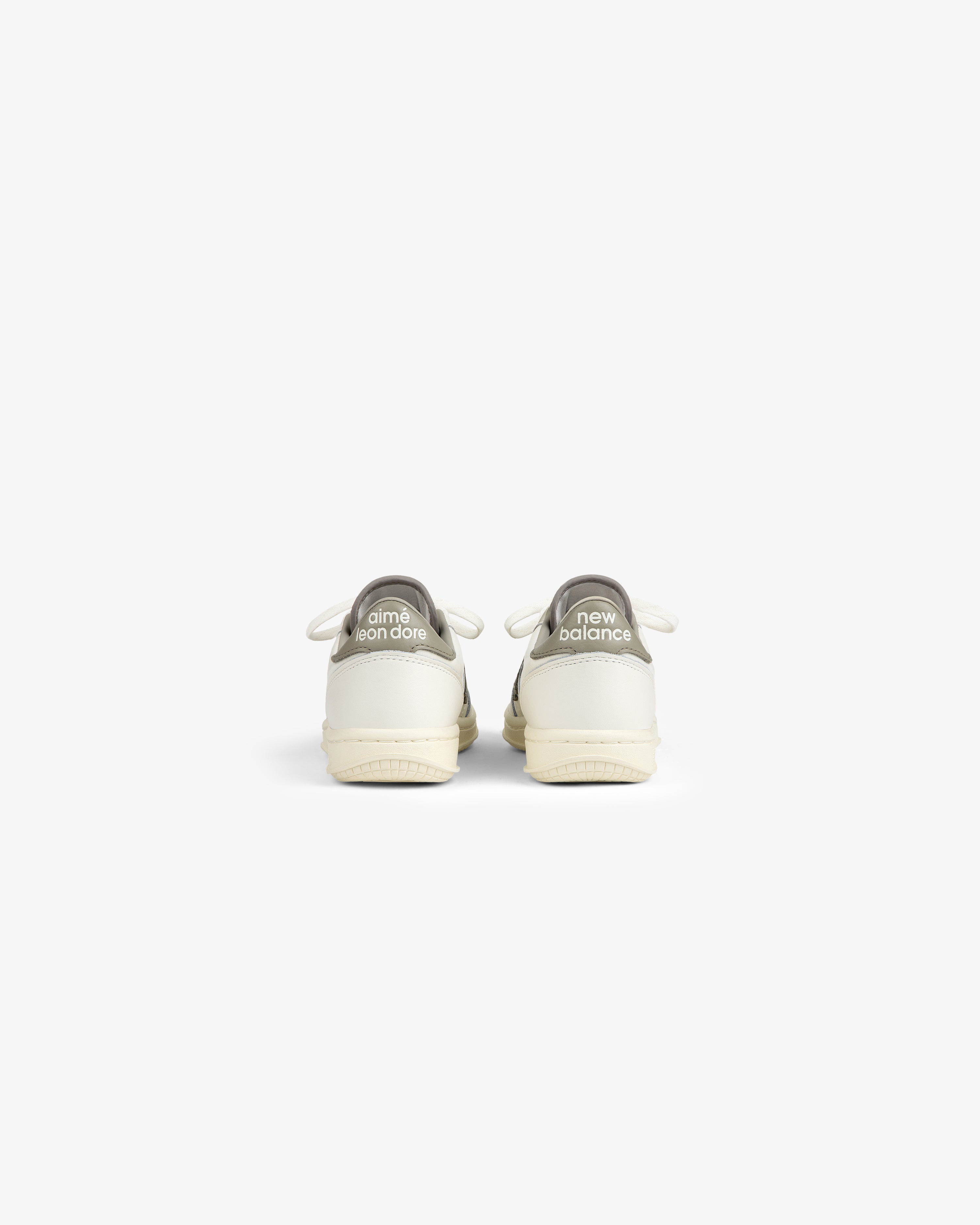 Back view of two white ALD / New Balance T500 Tennis Oxfords with grey heel tabs featuring logo text.