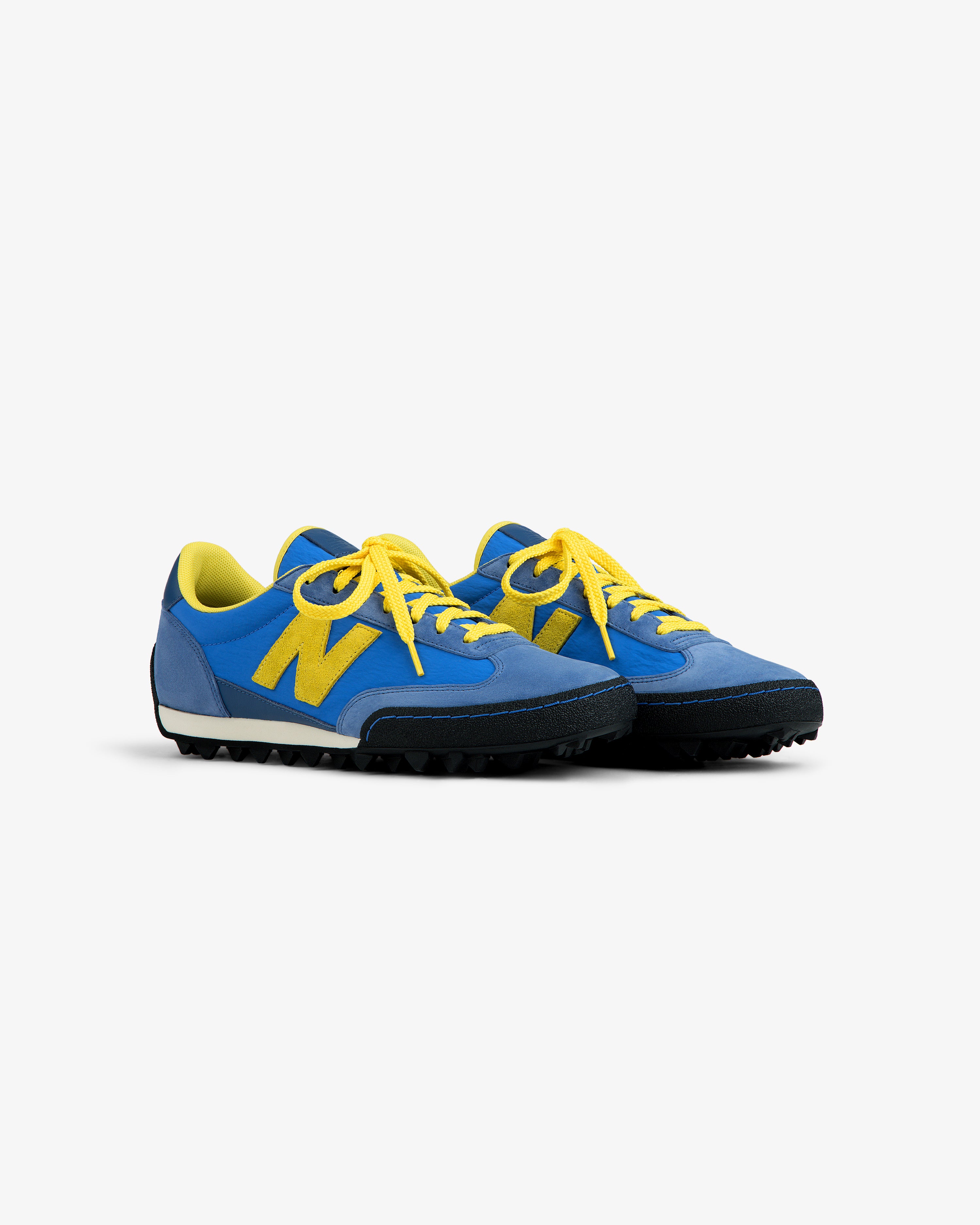 ALD / New Balance Gator blue low-top sneakers with yellow laces, logo, and a black textured rubber sole.