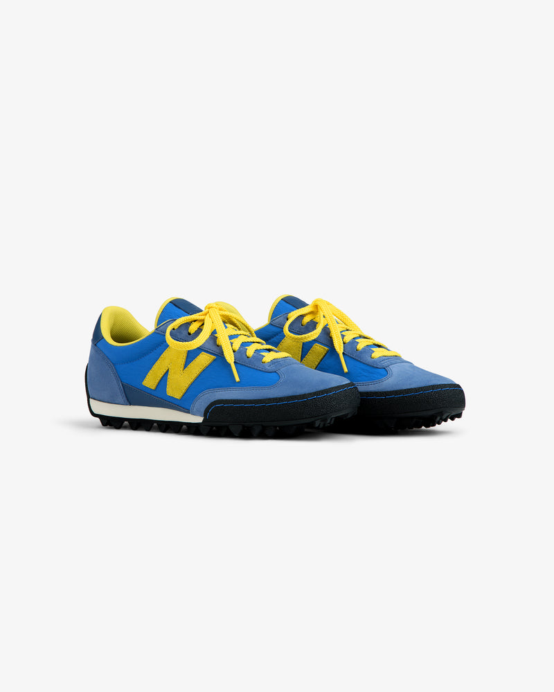 ALD / New Balance Gator blue low-top sneakers with yellow laces, logo, and a black textured rubber sole.