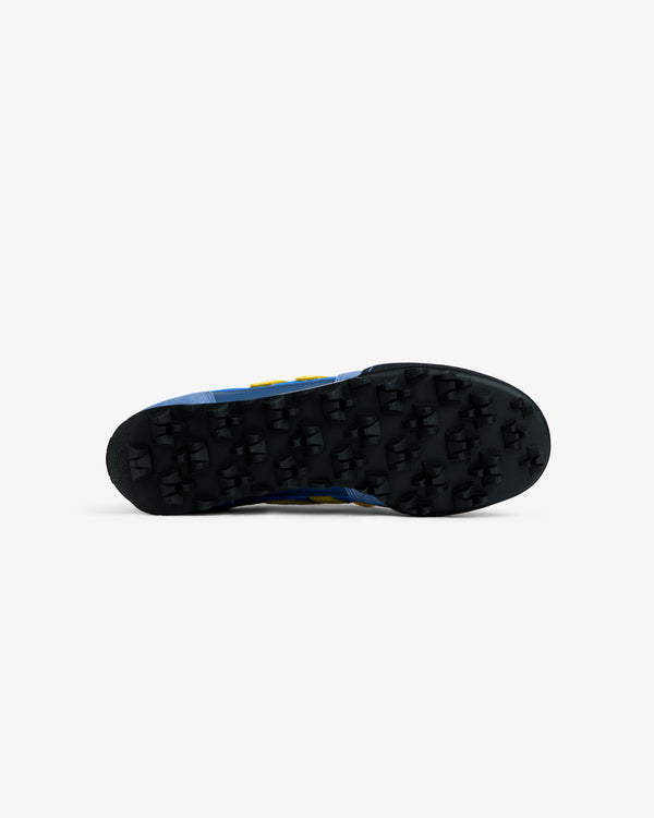 Black lugged rubber outsole of a blue ALD / New Balance Gator athletic shoe with yellow accents.