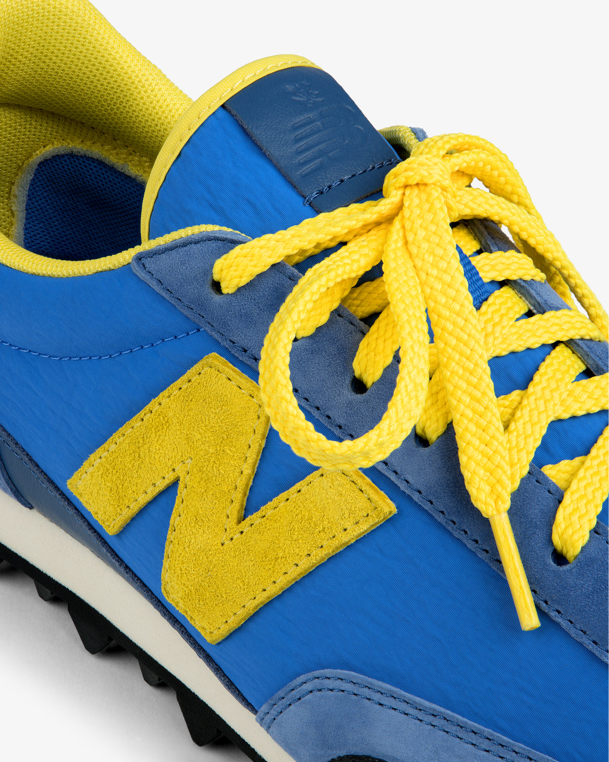 Close-up of an ALD / New Balance Gator sneaker in blue and yellow with a large yellow N logo and yellow laces.