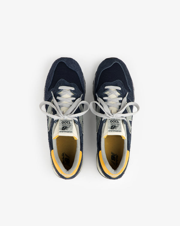 The ALD / New Balance Made in USA 1300 sneakers in navy blue and yellow, seen from above on a white background.