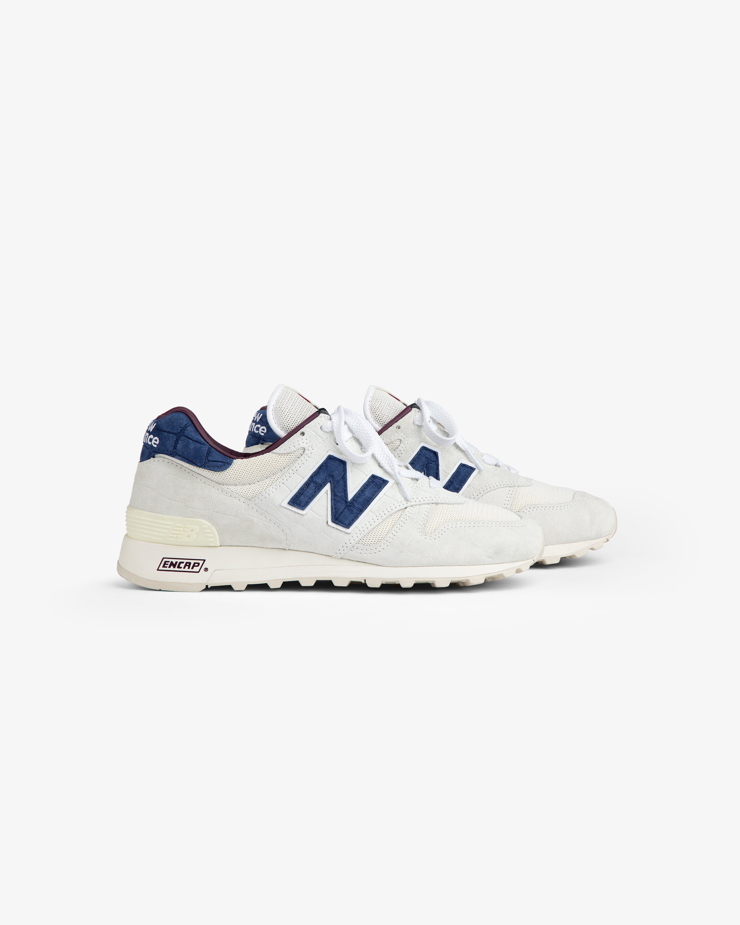 New Balance Made in USA 1300 sneakers, white and blue with laces, side view on plain white background.
