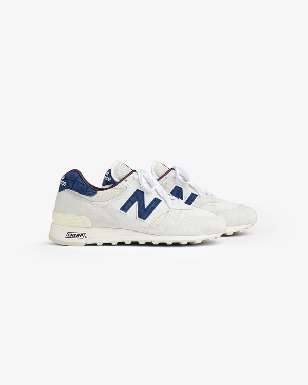 New Balance Made in USA 1300 sneakers, white and blue with laces, side view on plain white background.
