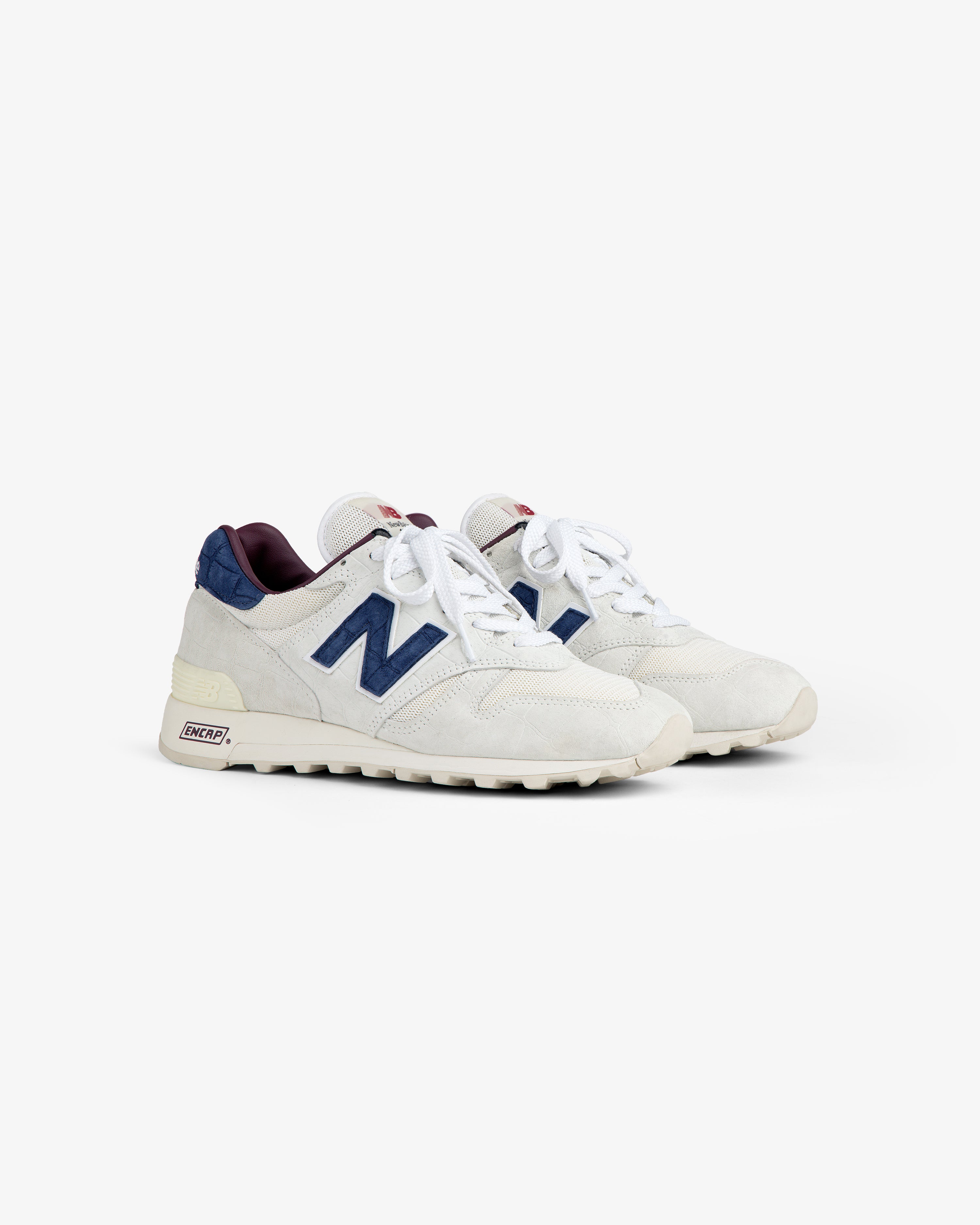 New Balance Made in USA 1300: white sneakers with navy N logo, maroon accents, off-white soles on white background.
