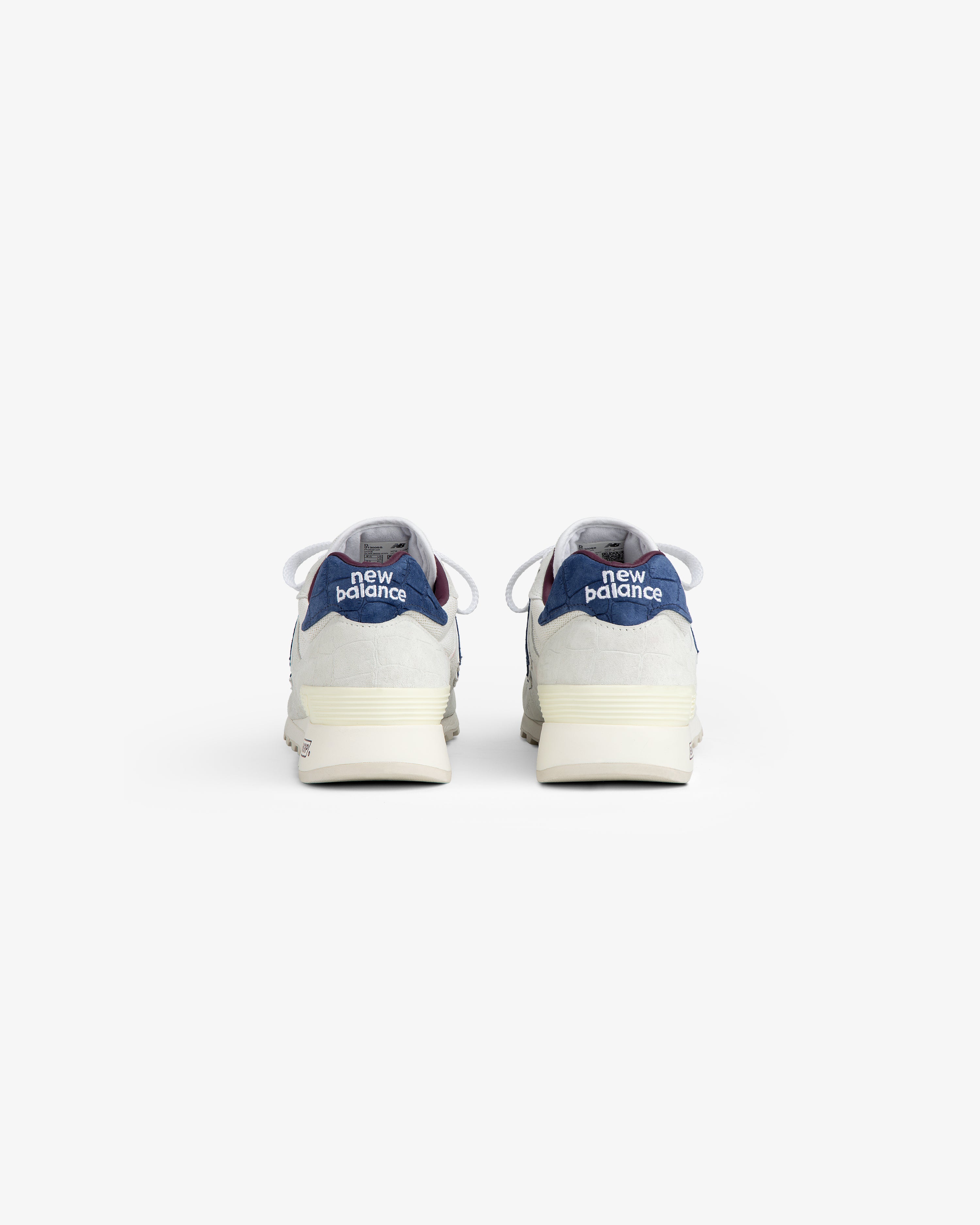New Balance Made in USA 1300 sneakers shown from the back, with blue and grey accents on a white background.