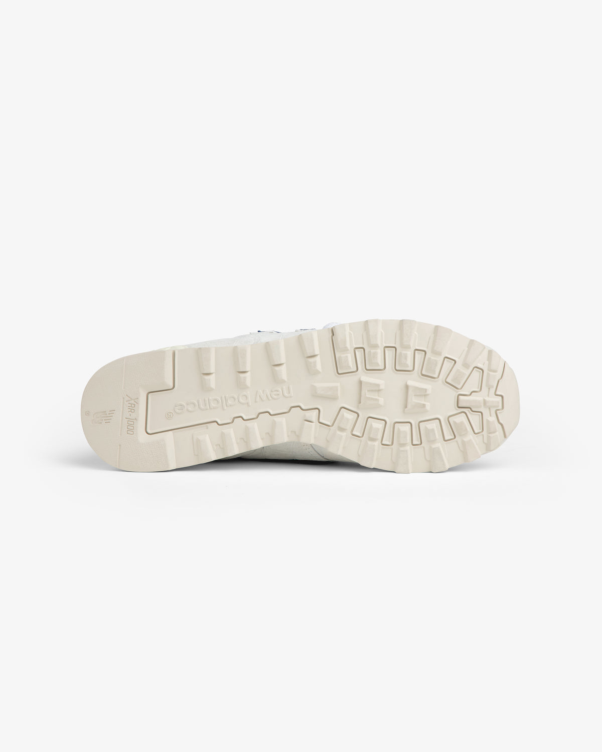 Sole of the New Balance Made in USA 1300 sneaker, beige with rugged tread, shown bottom-up against white background.