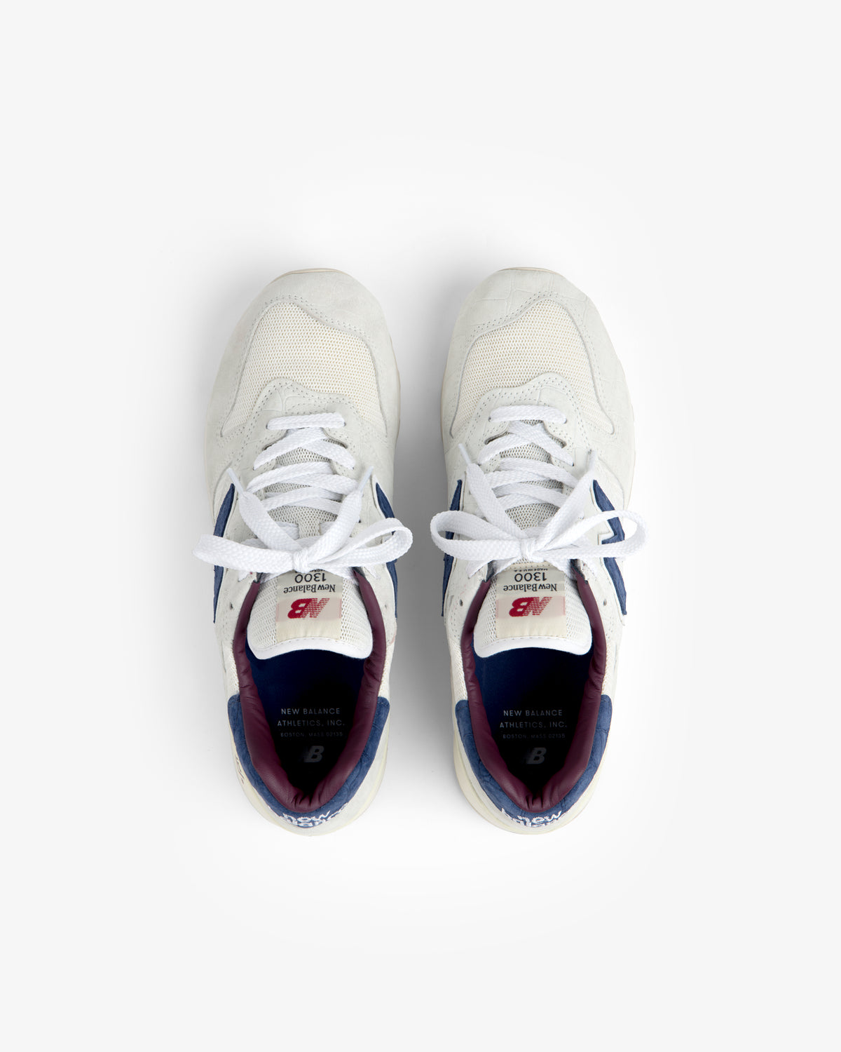 New Balance Made in USA 1300 sneakers in white with blue and maroon accents, shown from above on a white background.