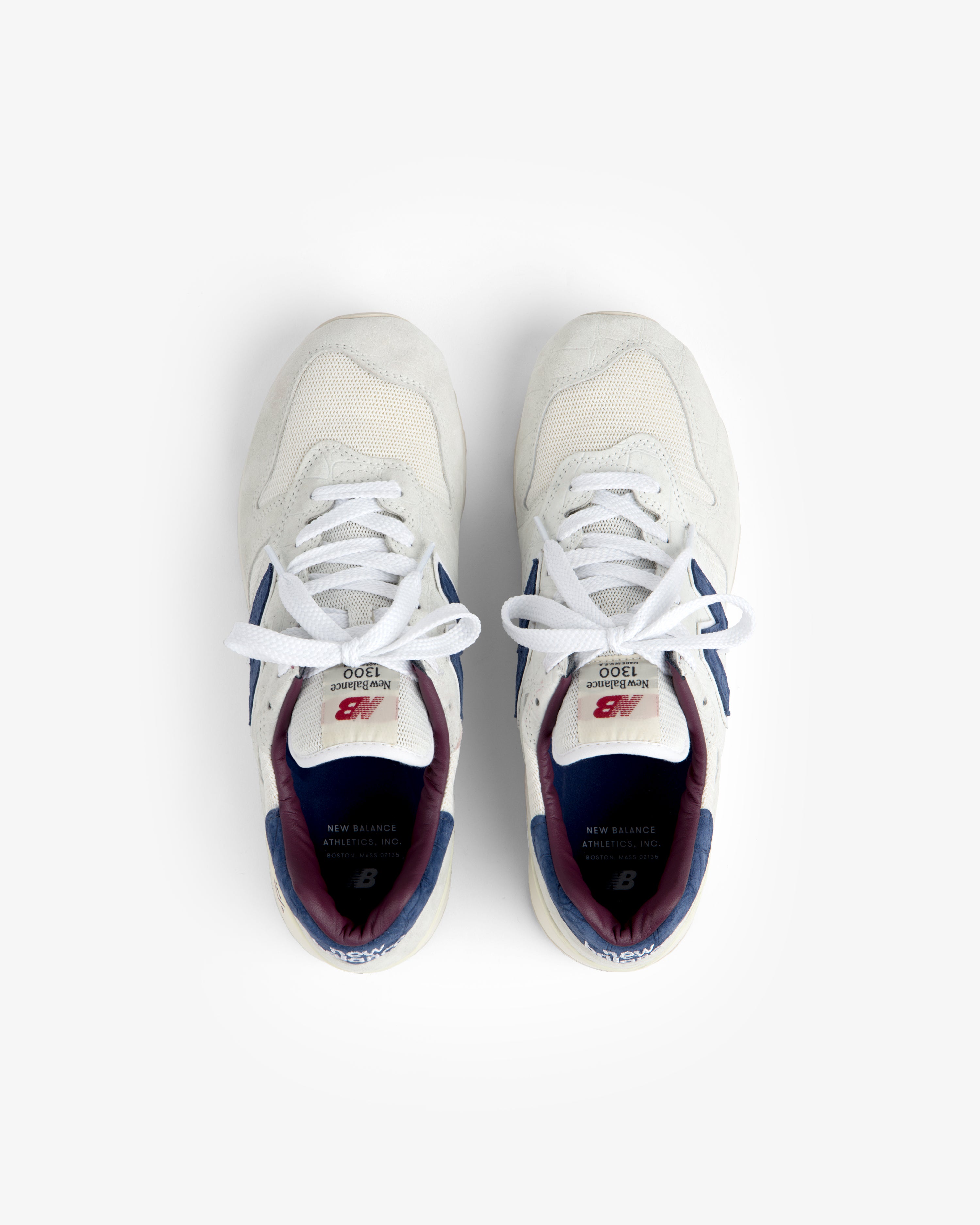New Balance Made in USA 1300 sneakers in white with blue and maroon accents, shown from above on a white background.