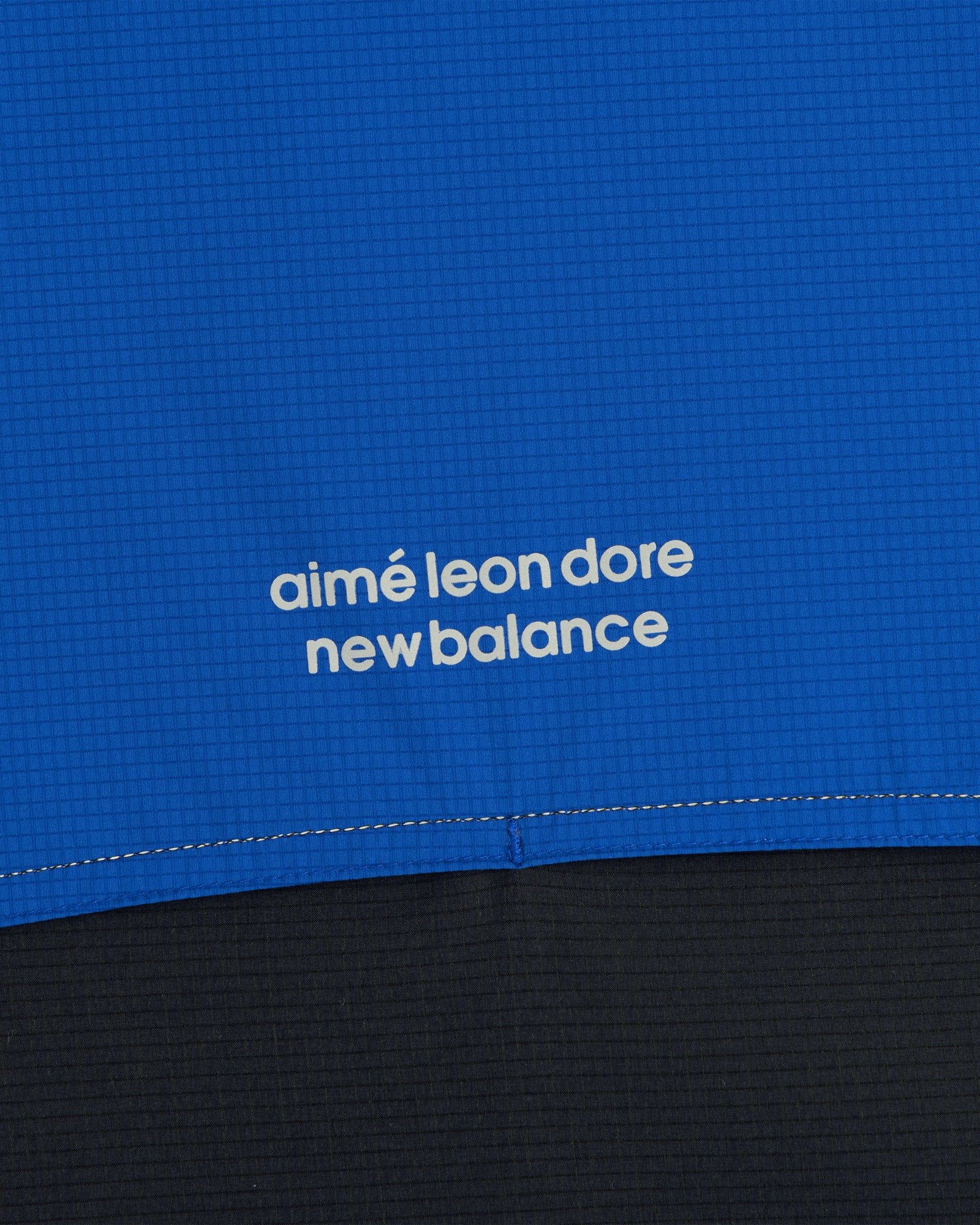 Close-up of blue ALD / New Balance Performance Nylon Jacket with white logo in lowercase letters.