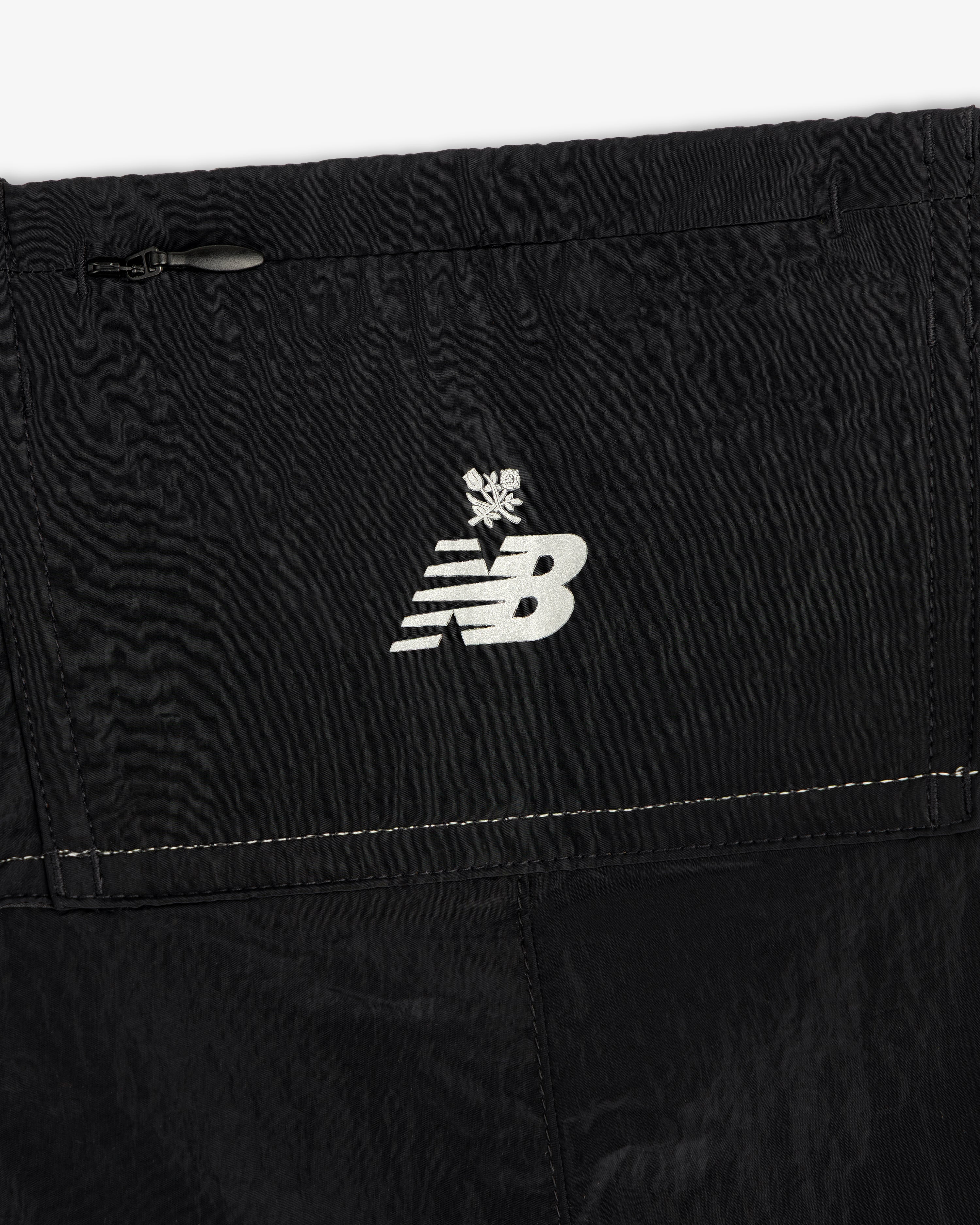 Close-up of the ALD / New Balance Lightweight Nylon Warmup Pant featuring a white logo and snowflake on black fabric.
