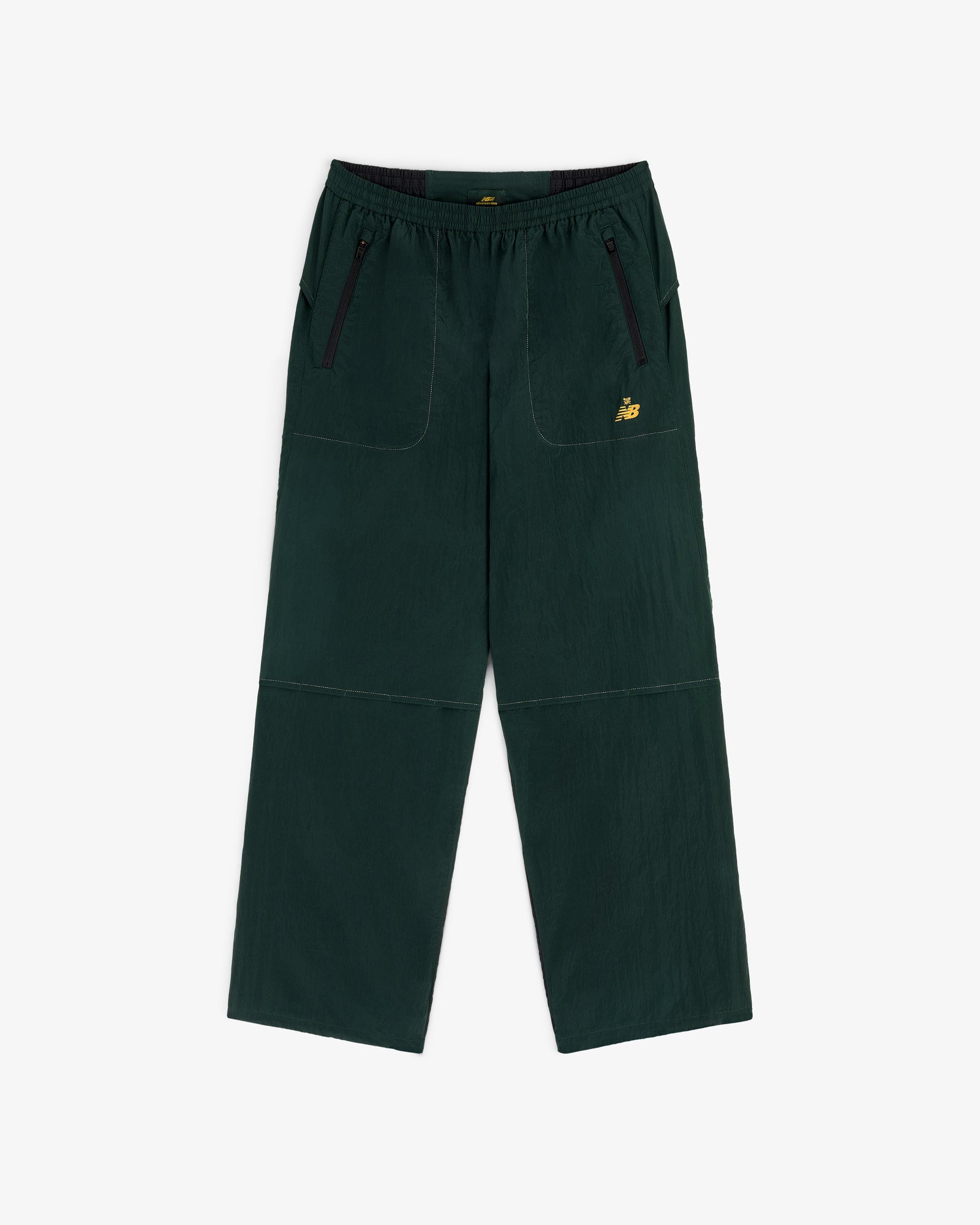ALD / New Balance Lightweight Nylon Warmup Pant in dark green with front pockets, black zippers, and yellow NB logo.