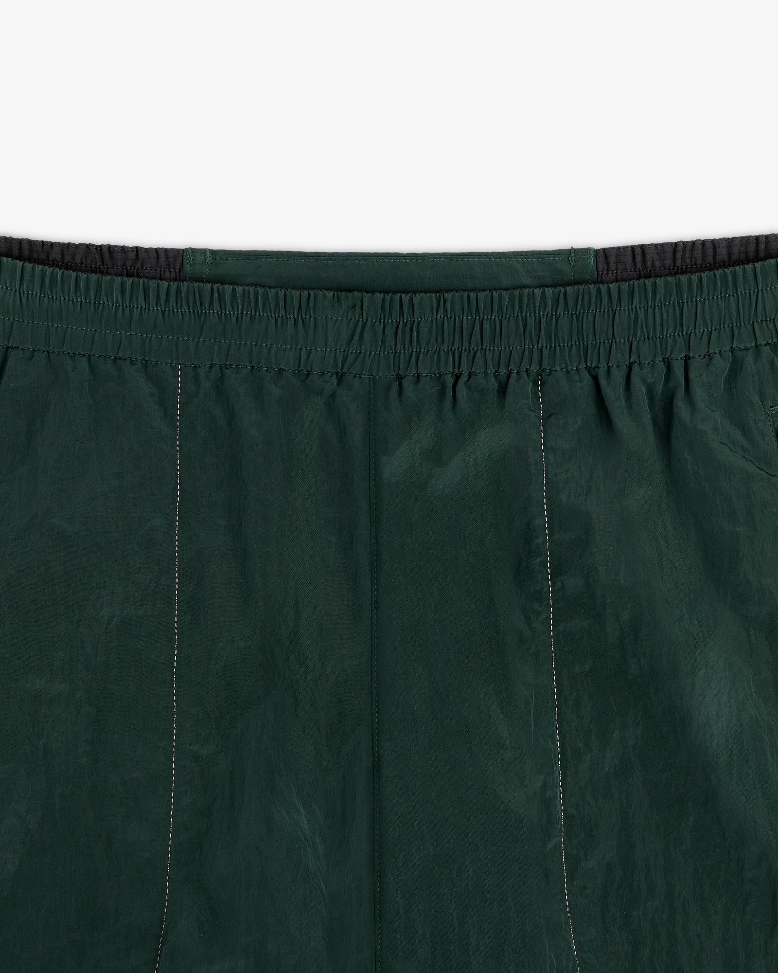 Close-up of the waistband and upper section of the ALD / New Balance Lightweight Nylon Warmup Pant in dark green.