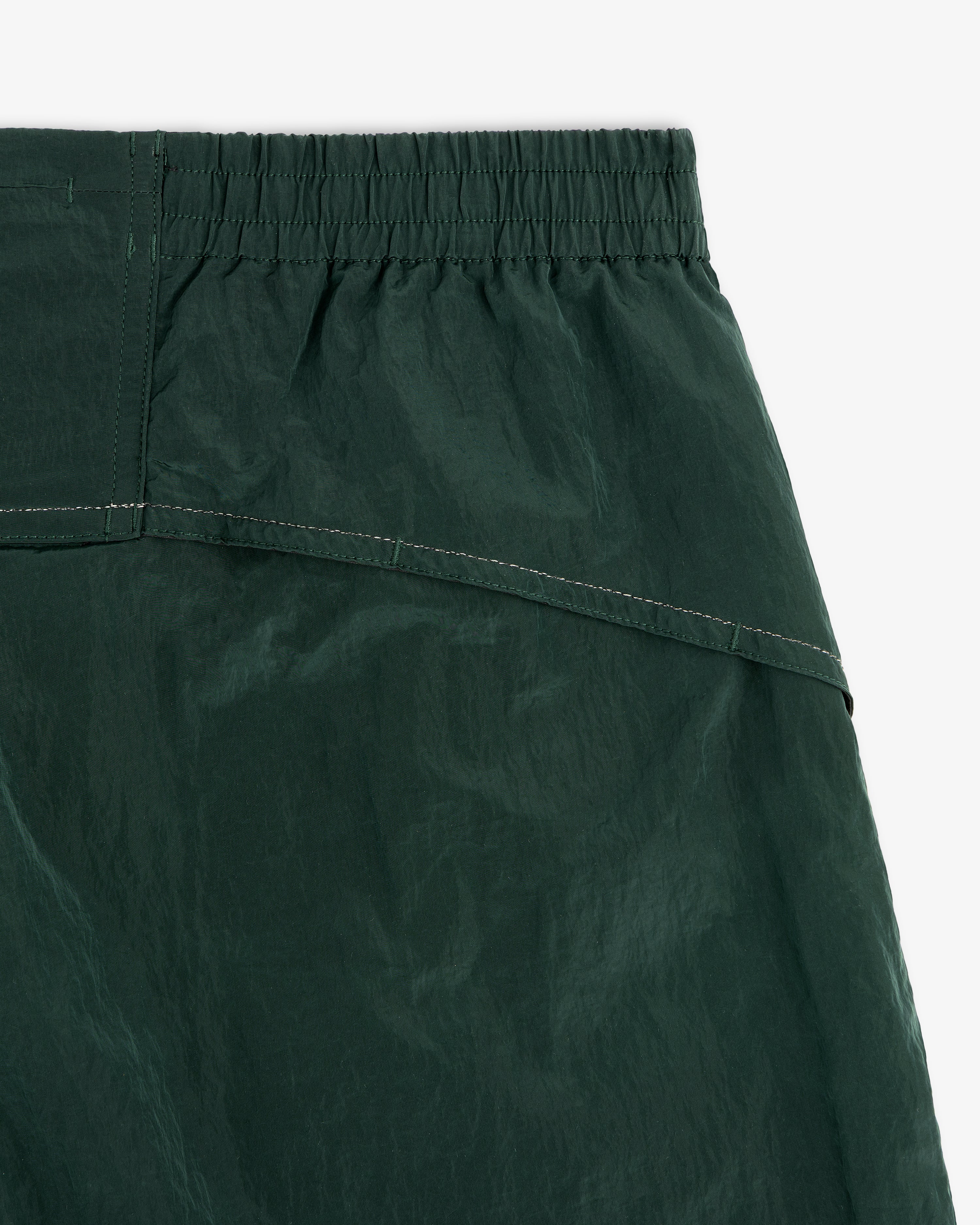 Close-up of ALD / New Balance Lightweight Nylon Warmup Pant in forest green with elastic waistband and visible stitching.