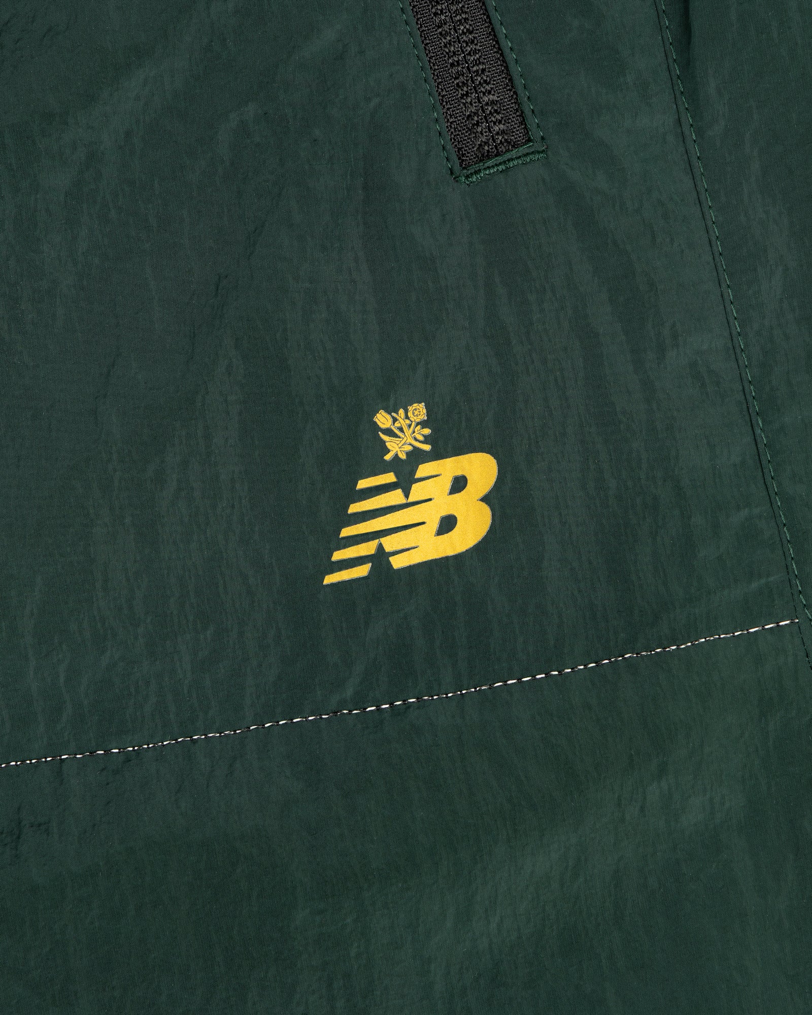 Close-up of ALD / New Balance Lightweight Nylon Warmup Pant in green with yellow NB logo, crown, seam, and zipper.