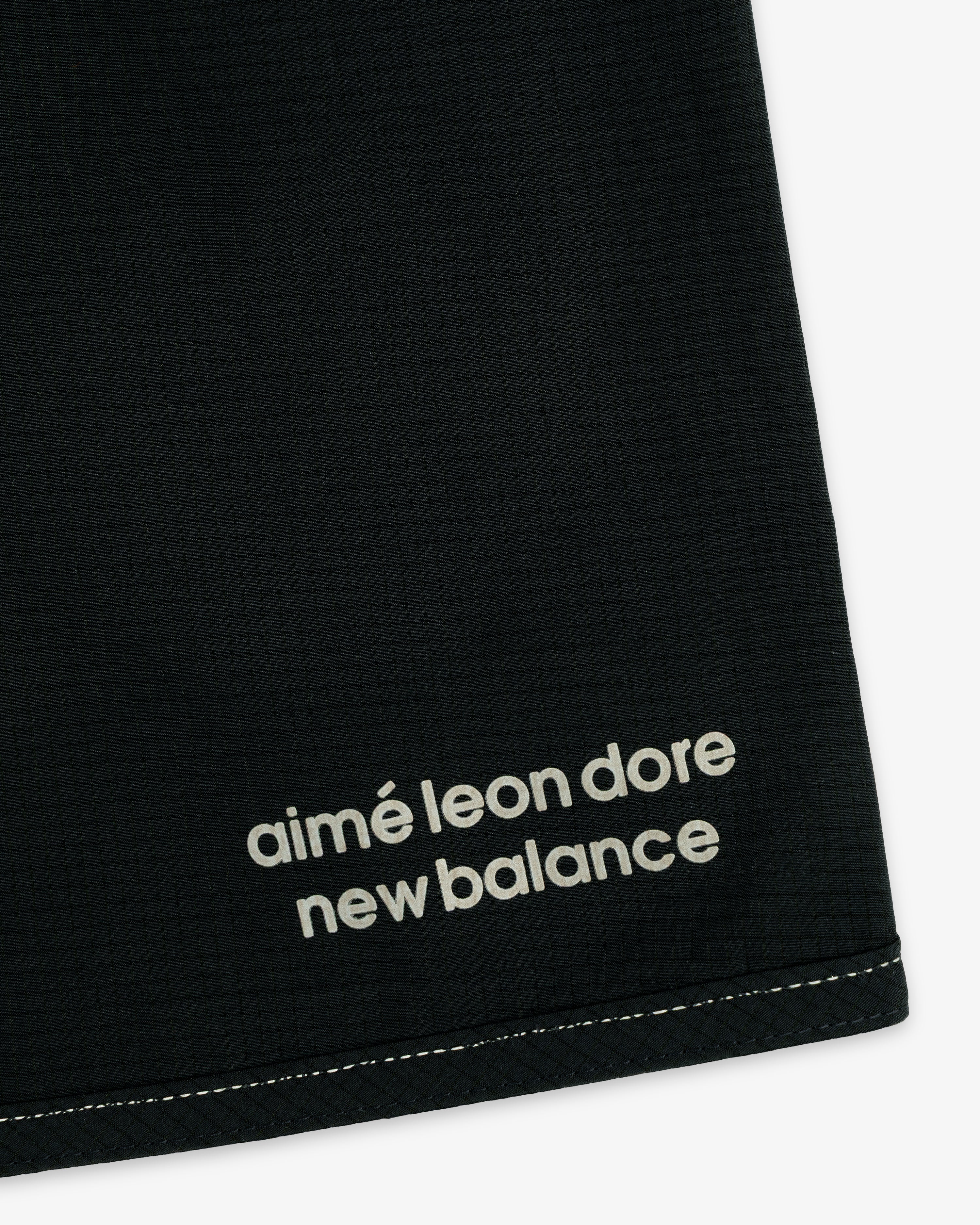 Close-up of black ALD / New Balance Performance Lightweight Running Short with white logo near hem and visible stitching.