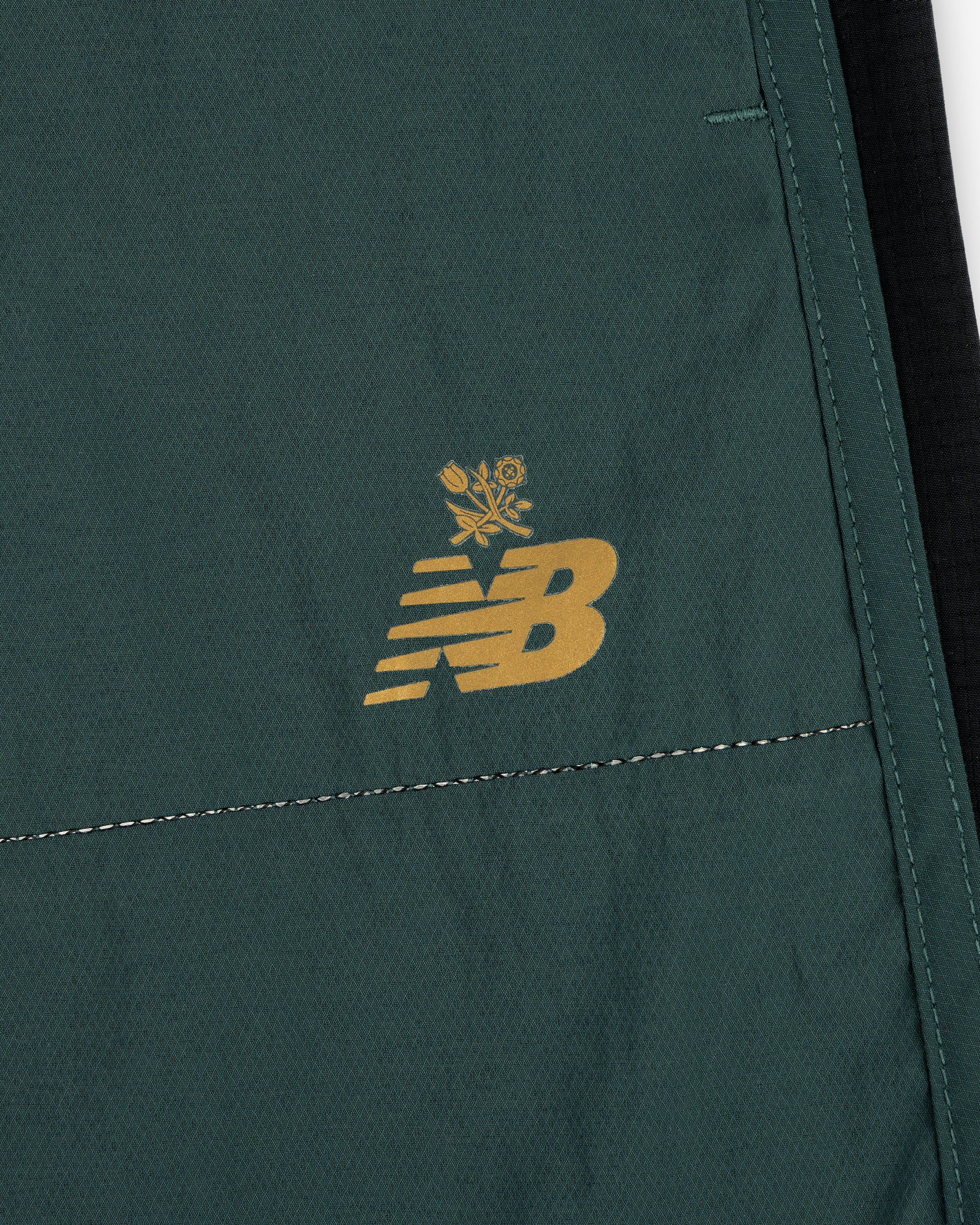 Close-up of green ALD / New Balance Performance Lightweight Running Short with yellow logo and small floral graphic.