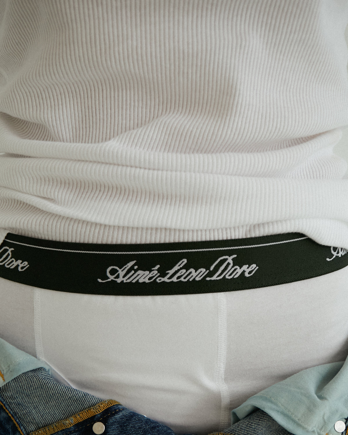 Close-up of a person wearing a white ribbed shirt and Boxer Brief 3-Pack with Aimé Leon Dore on the waistband.