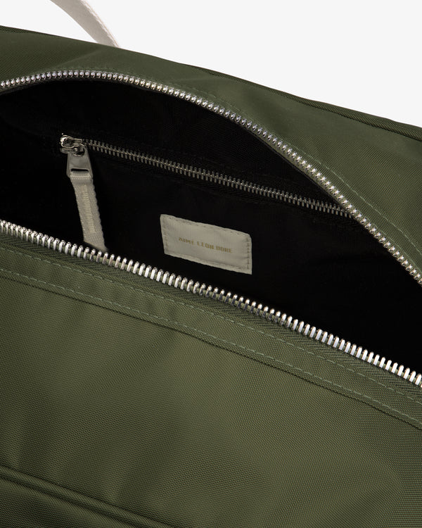 Close-up of an open Nylon Duffle Bag in olive green with a silver zipper, showing interior zip pocket and label.