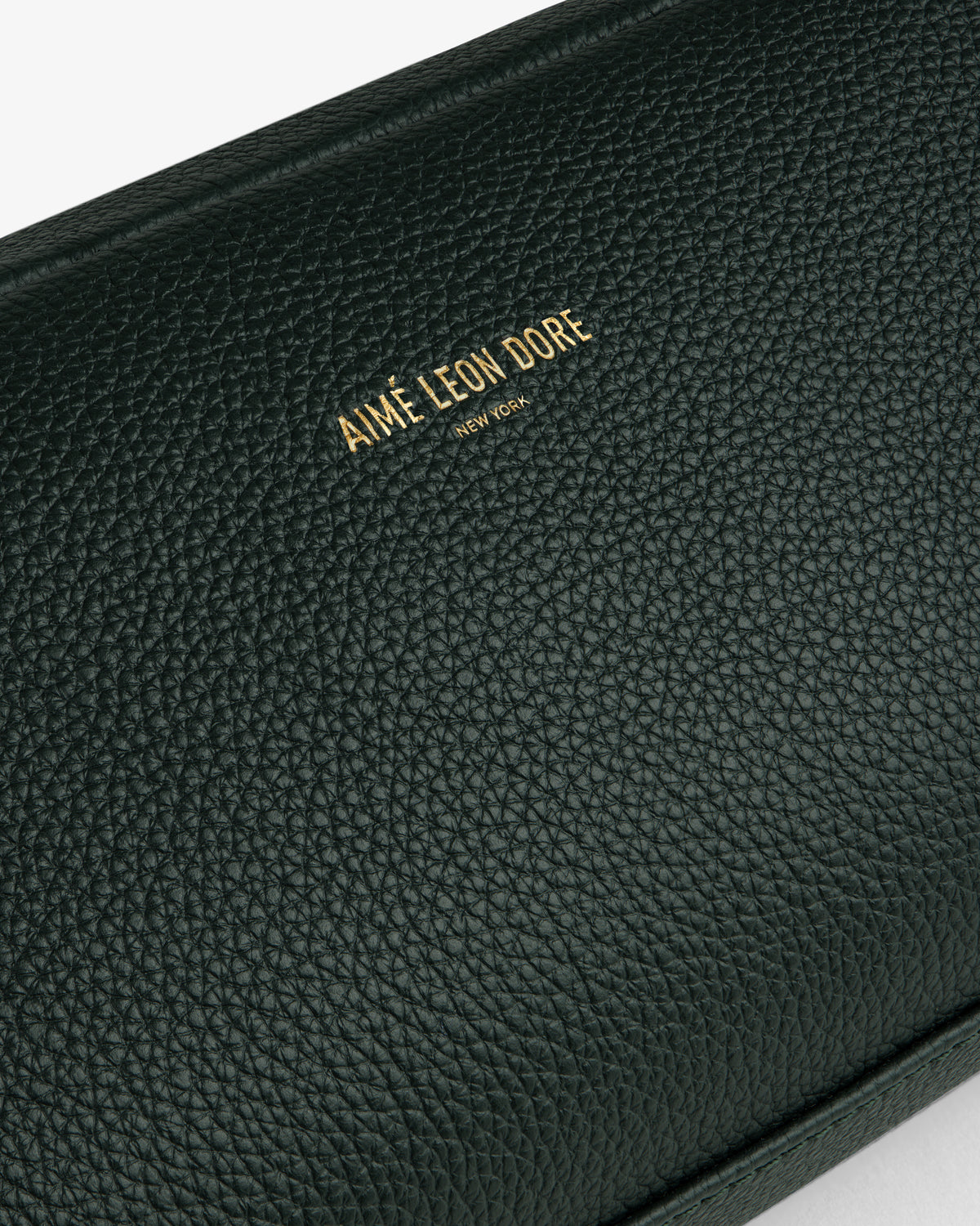 Close-up of a textured dark green Leather Traveler Kit with gold Aimé Leon Dore New York branding embossed.