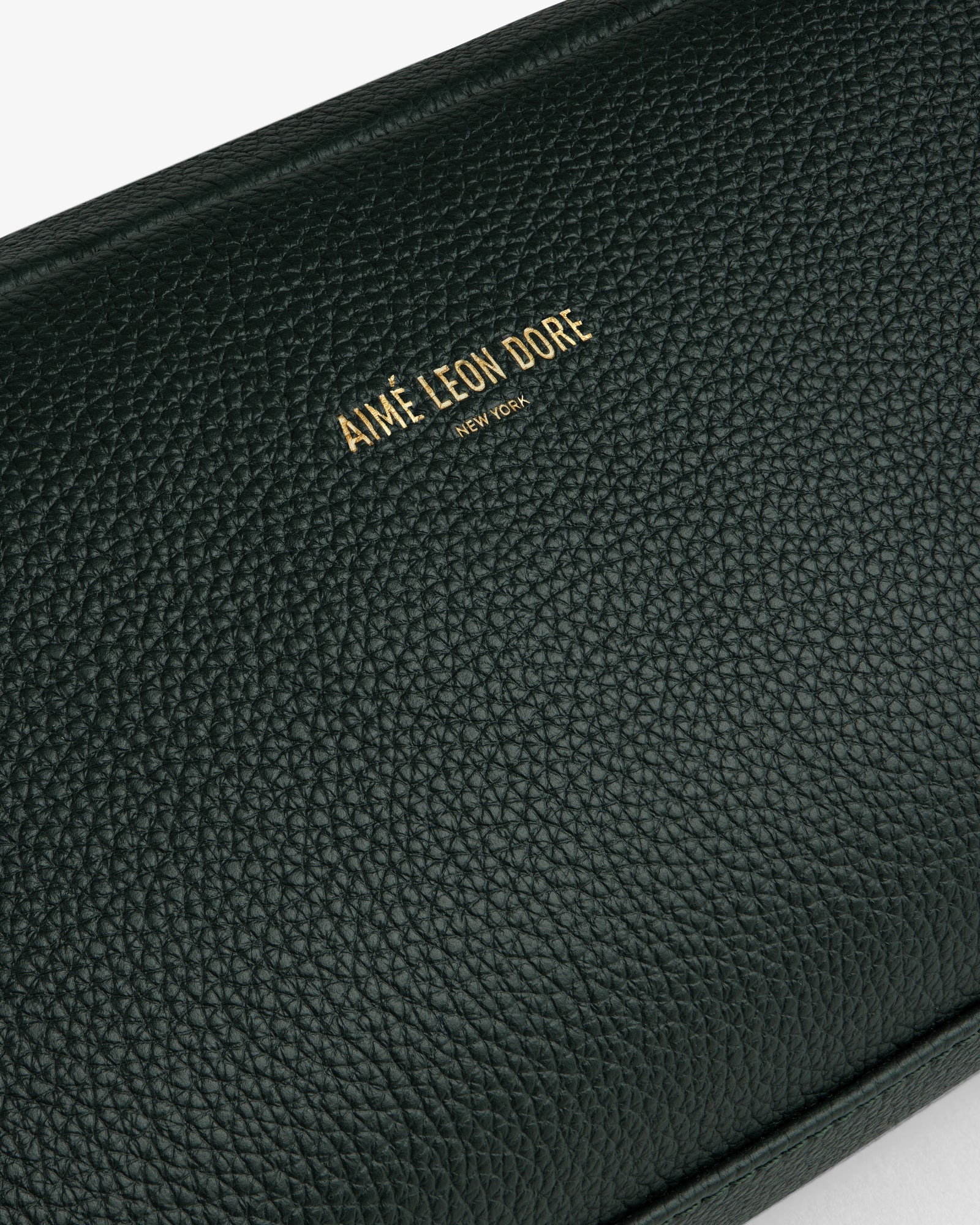 Close-up of a textured dark green Leather Traveler Kit with gold Aimé Leon Dore New York branding embossed.