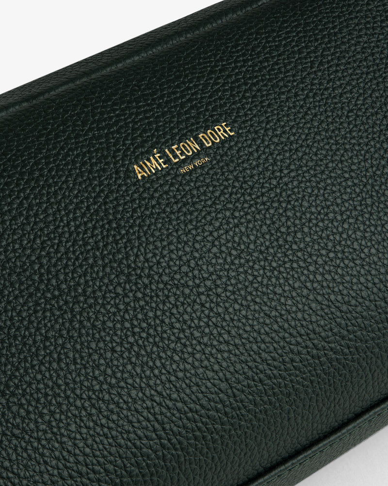 Close-up of a textured dark green Leather Traveler Kit with gold Aimé Leon Dore New York branding embossed.