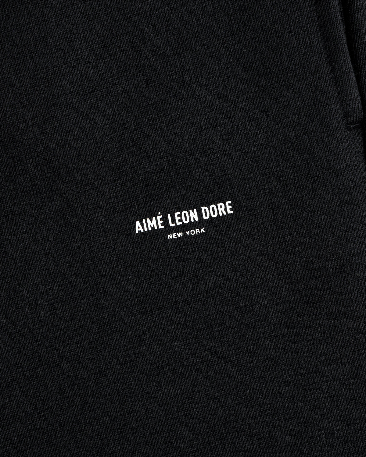 Close-up of black Micro Logo Sweatpants with AIMÉ LEON DORE NEW YORK printed in small white letters.
