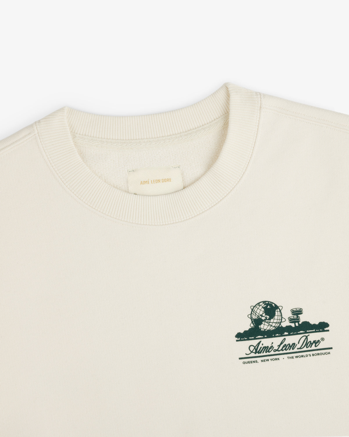 Cream Unisphere Crewneck Sweatshirt with small green graphic and Aimé Leon Dore text on the left chest.