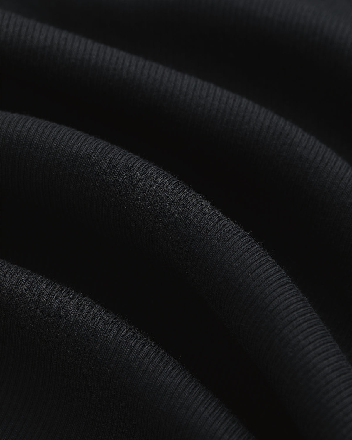 Close-up of black ribbed Tank Top 3-Pack fabric with soft folds and visible textured lines.