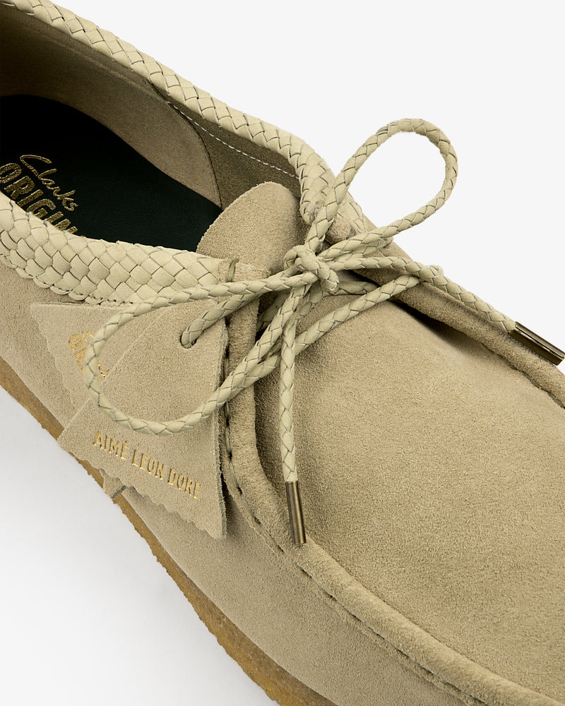 Close-up of a beige ALD / Clarks Suede Wallabee with braided laces and gold AIME LEON DORE text on the tag.