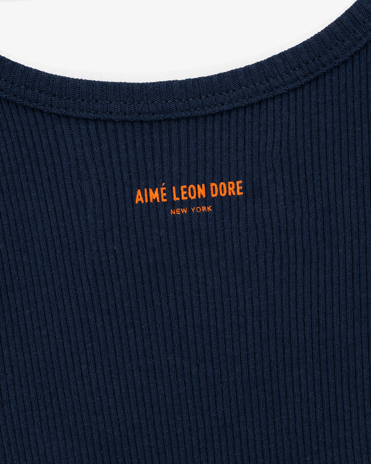 Close-up of the Mets Tank Top in navy ribbed fabric with orange AIMÉ LEON DORE NEW YORK text near the collar.