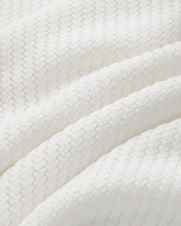 Close-up of a white, textured Pointelle Knit Sweater with soft diagonal folds under gentle lighting.